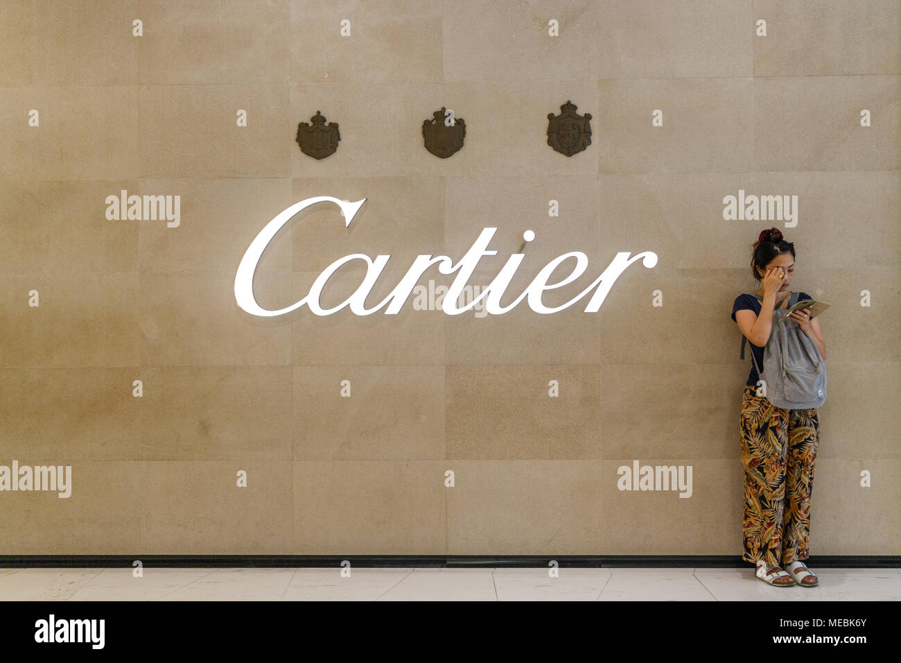 Eine Frau überprüft Ihr Telefon außerhalb ein Cartier shop, Emporium Shopping Mall, Bangkok, Thailand Stockfoto