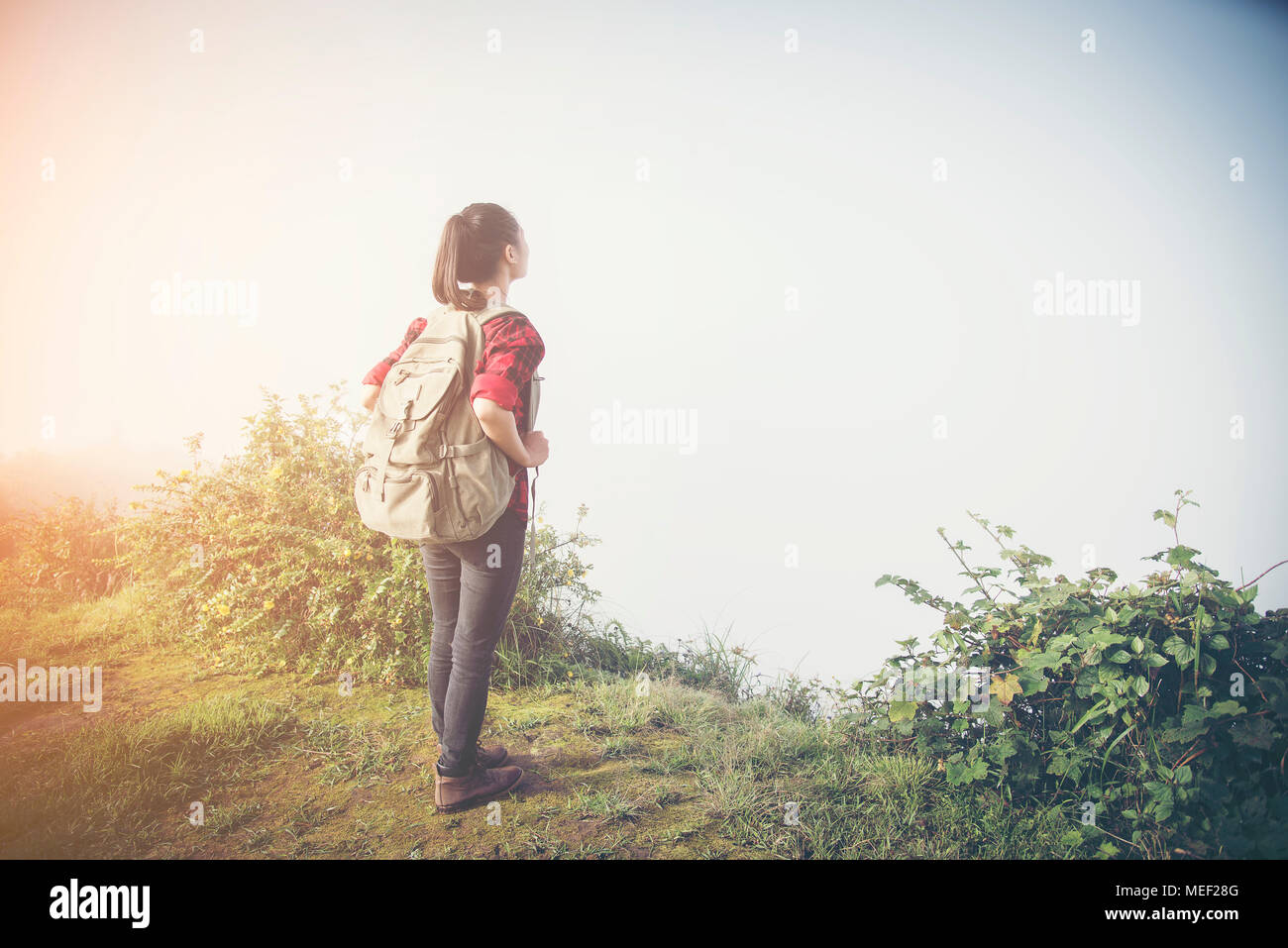 Hipster junges Mädchen mit Rucksack Sonnenuntergang am Gipfel des Foggy Mountain. Touristische Reisende auf Hintergrundansicht mockup. Wanderer, die Sonnenlicht in der Reise Stockfoto