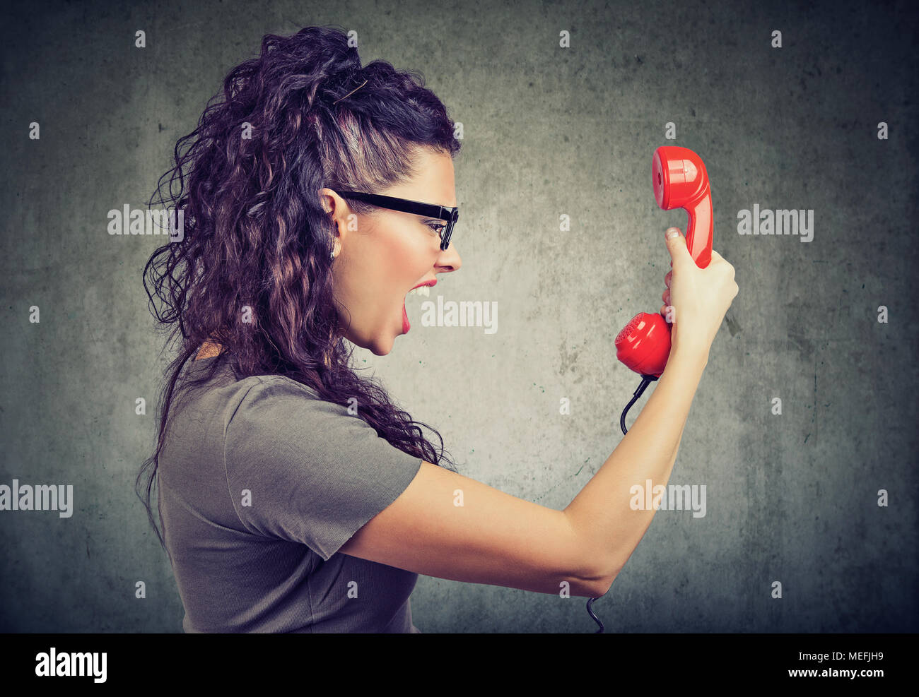 Seitenansicht der schönen Frau mit einem roten Telefonhörer und Schreien vor Wut. Stockfoto