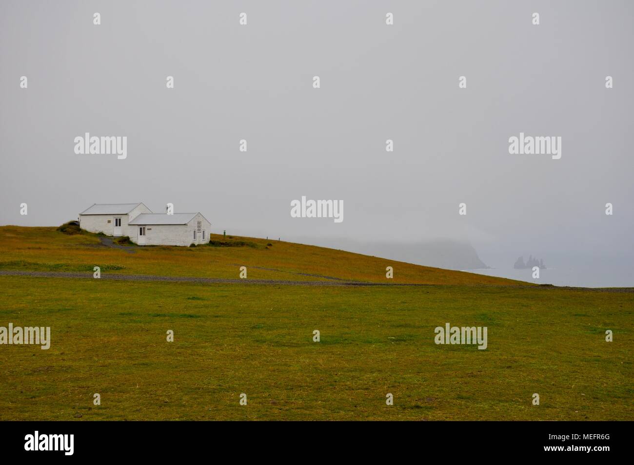 Weiße Hütte auf einem grasbewachsenen Hügel, Island Stockfoto