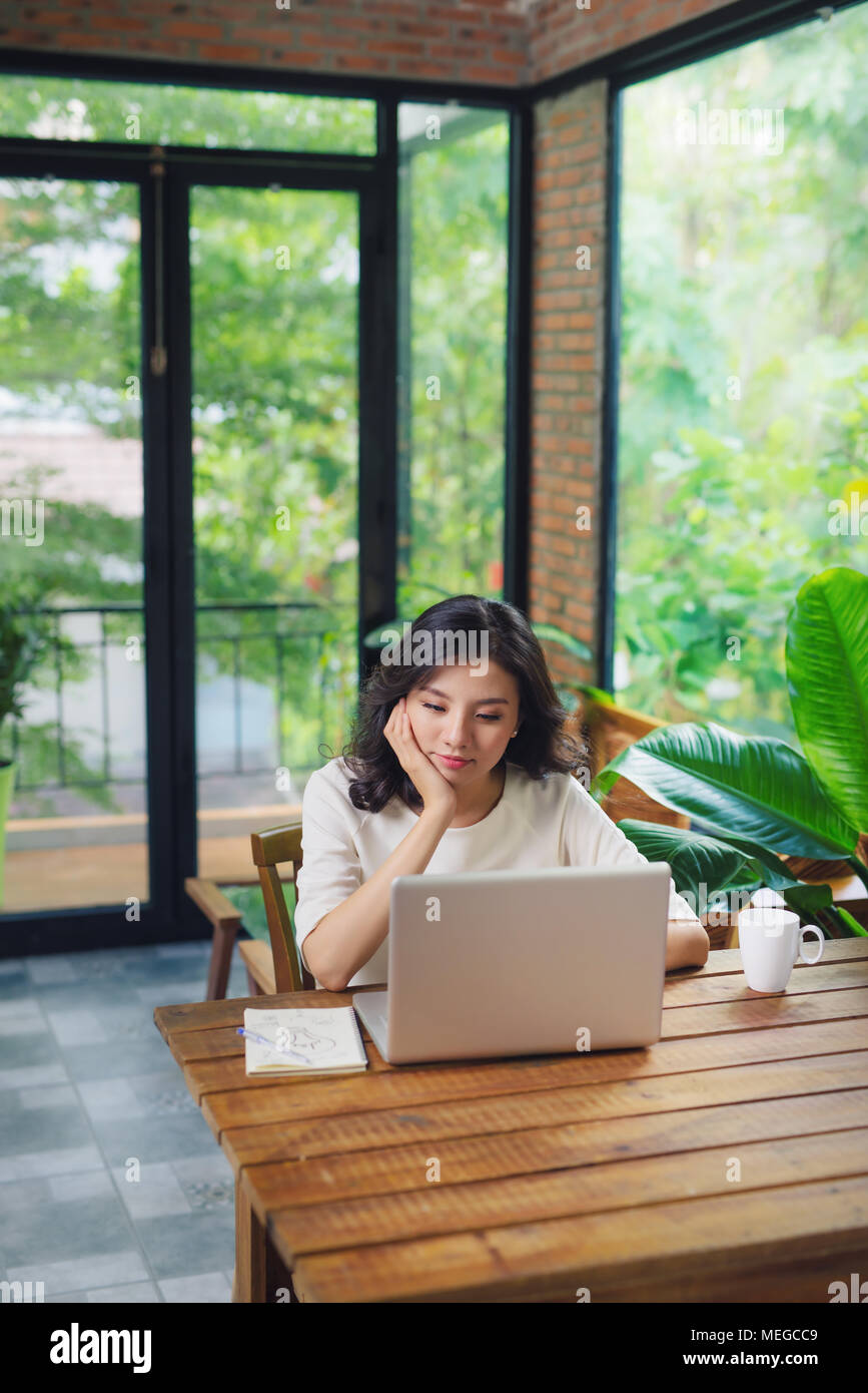 Schöne junge lächelnde Frau mit Laptop in der Nähe der grossen Fenster. Stockfoto