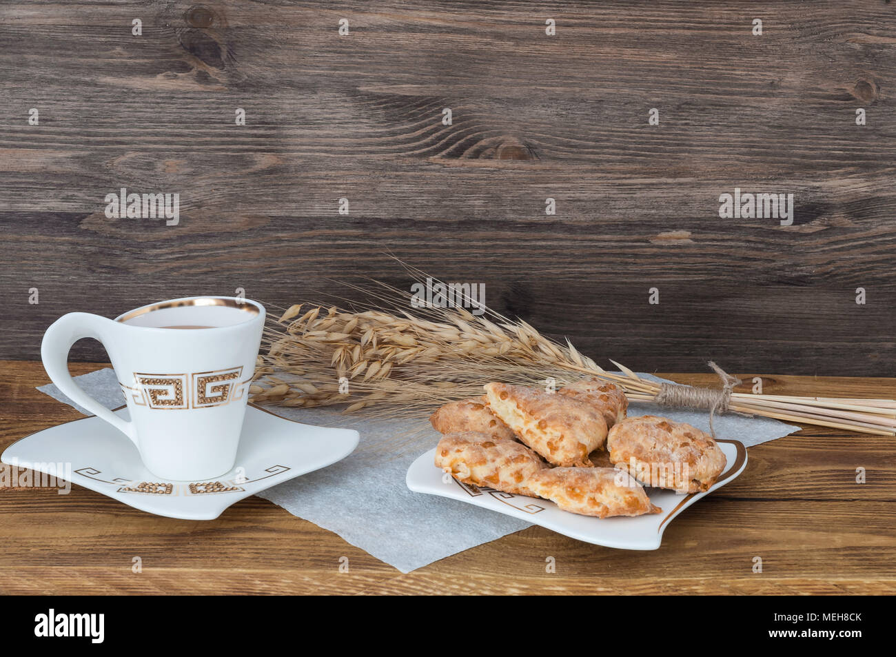 Eine Tasse Tee, hausgemachte Kekse und Weizenähren auf einem Hintergrund von Holzplatten. Stockfoto