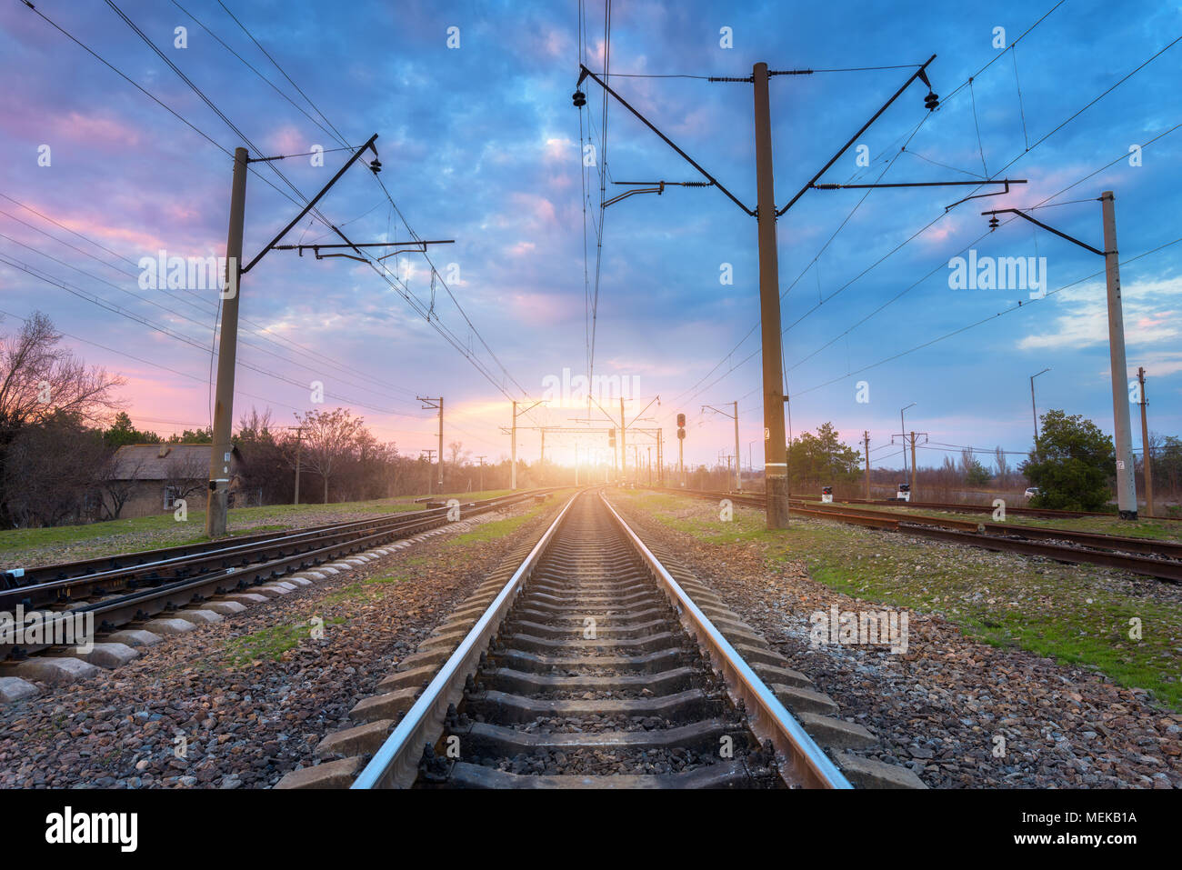 Eisenbahn und schönen Himmel bei Sonnenuntergang. Industrielle Landschaft mit Bahnhof, bunten blauen Himmel mit Wolken, Bäume und Gras, gelbe Sonnenlicht Stockfoto