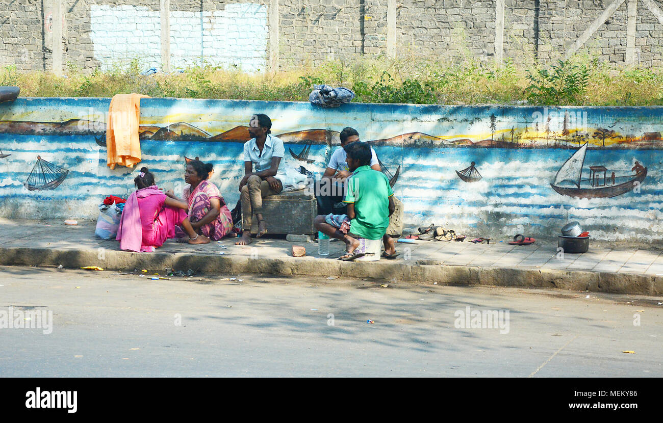 Eine Gruppe von Männern und Frauen saßen entspannen und unterhalten auf dem Gehweg auf einer Straße in Mumbai, Indien Stockfoto