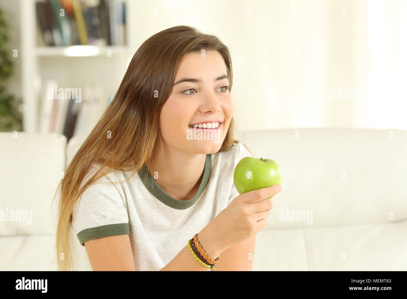 Happy Teen mit einem Apfel weg schauen sitzen auf einer Couch im Wohnzimmer zu Hause Stockfoto