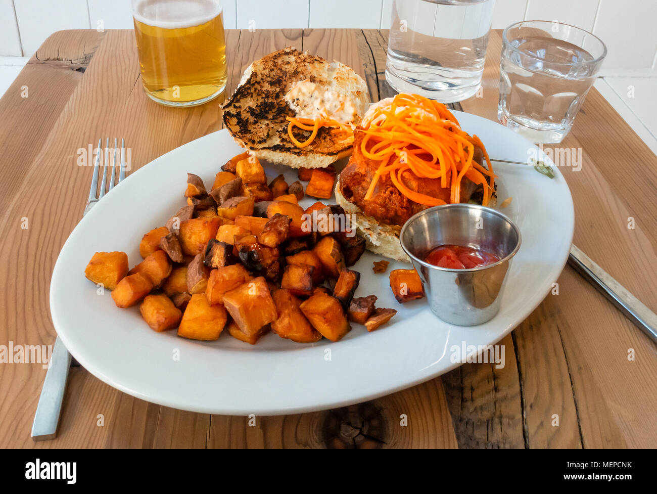 Ein weisser Fisch Sandwich auf einer Rolle mit Karotten Streifen und serviert mit würzigen gewürfelte Kartoffeln Stockfoto