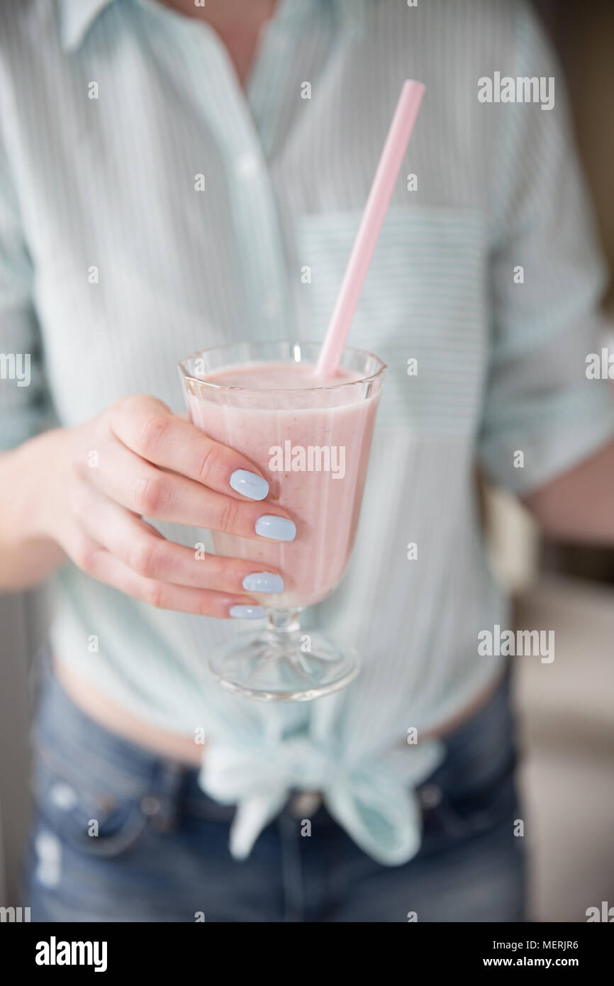 Im mittleren Abschnitt eine modische Mädchen mit Pastellfarben und halten ein volles Glas der Erdbeere Smoothie oder Milchshake mit einem rosa Stroh Stockfoto