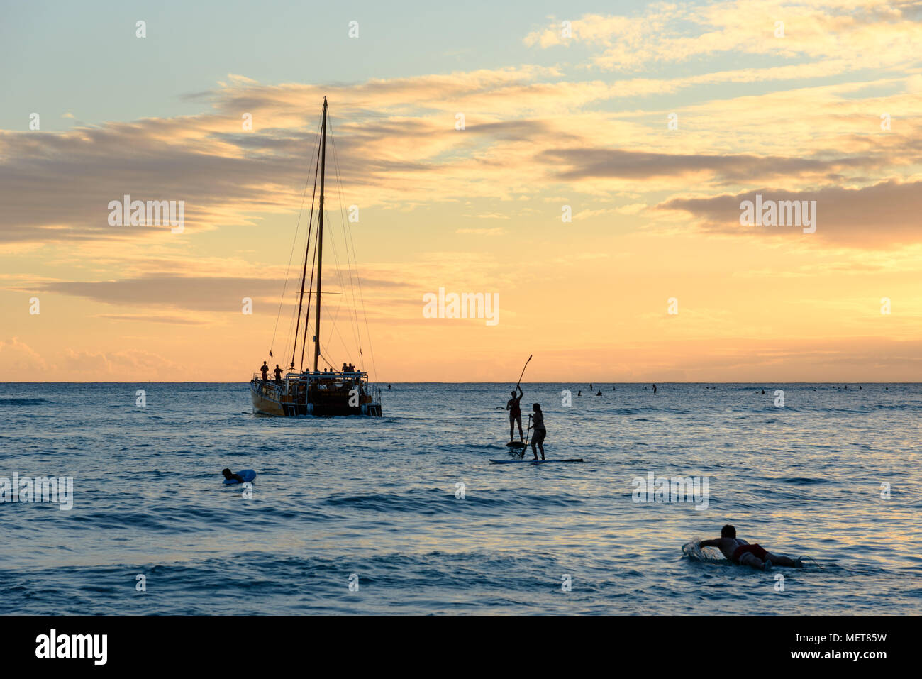 Ein Segelboot und standup paddleboarders bei Sonnenuntergang am Waikiki Beach, Hawaii Stockfoto