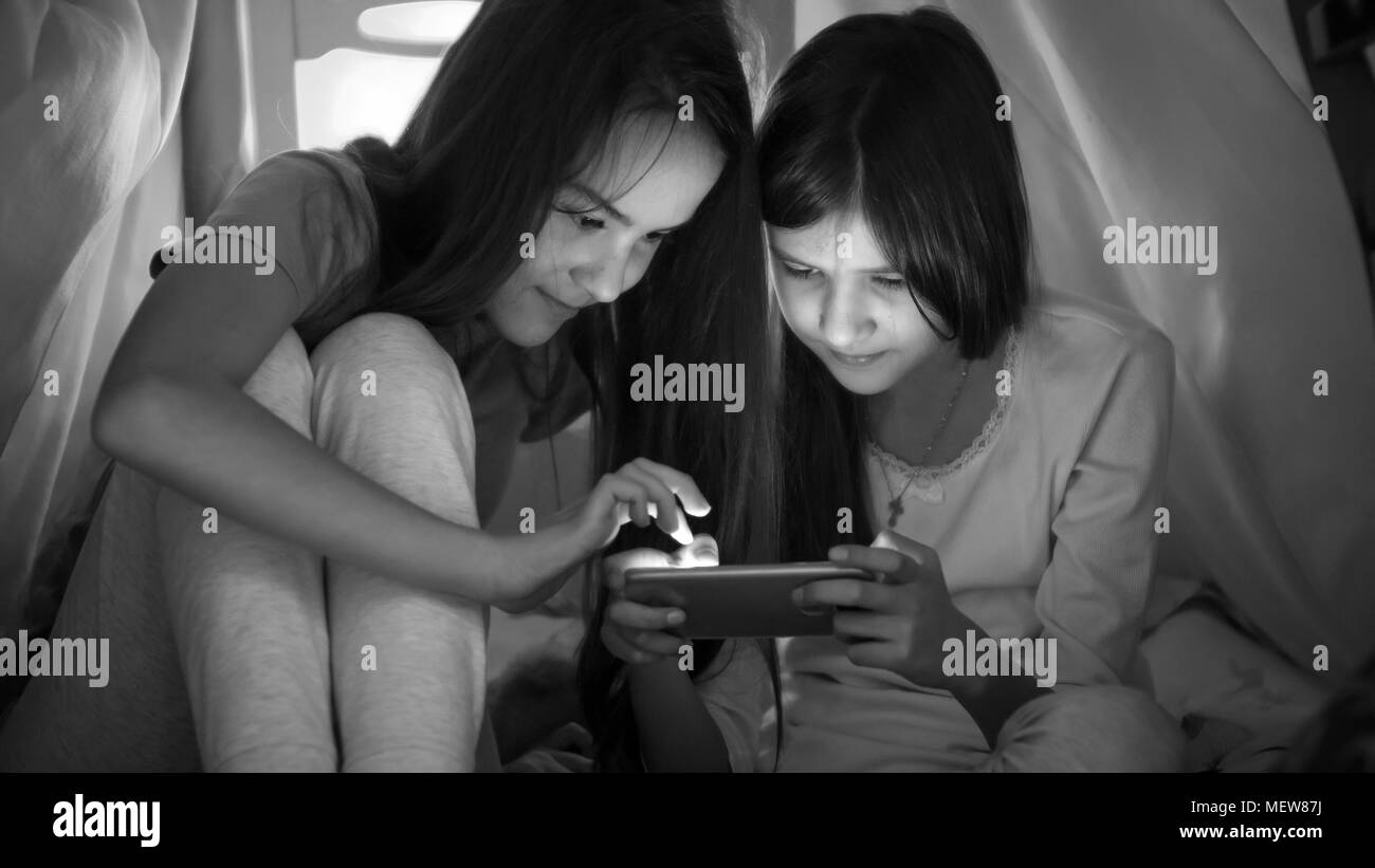 Schwarz-weiß Foto von zwei Mädchen im Teenager-Alter spielen auf Handy bei Nacht Stockfoto