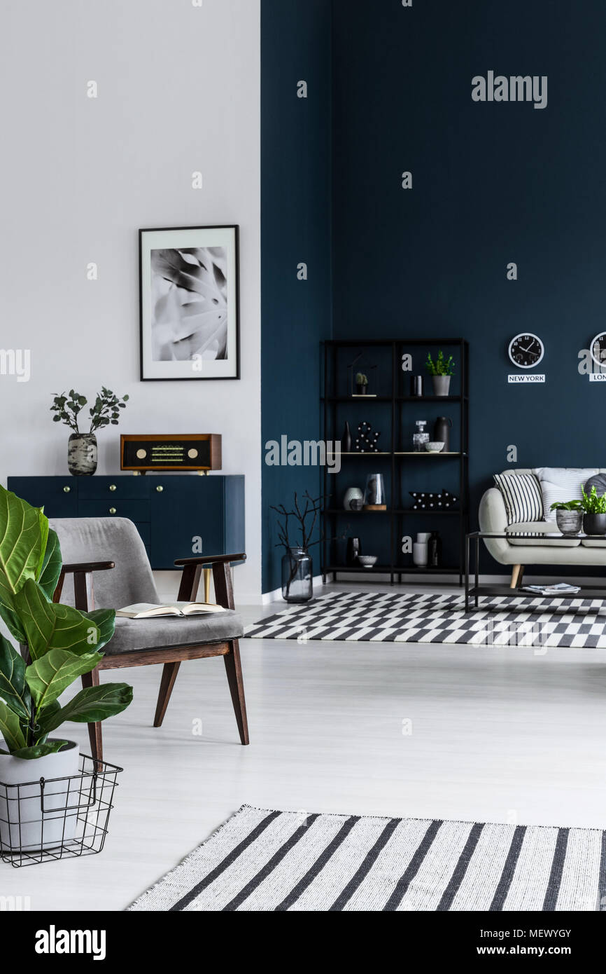 Dunkle Wohnzimmer Einrichtung mit Sessel, Pflanze, gestreifte Teppiche, Metall Regal und Sofa im Hintergrund Stockfoto