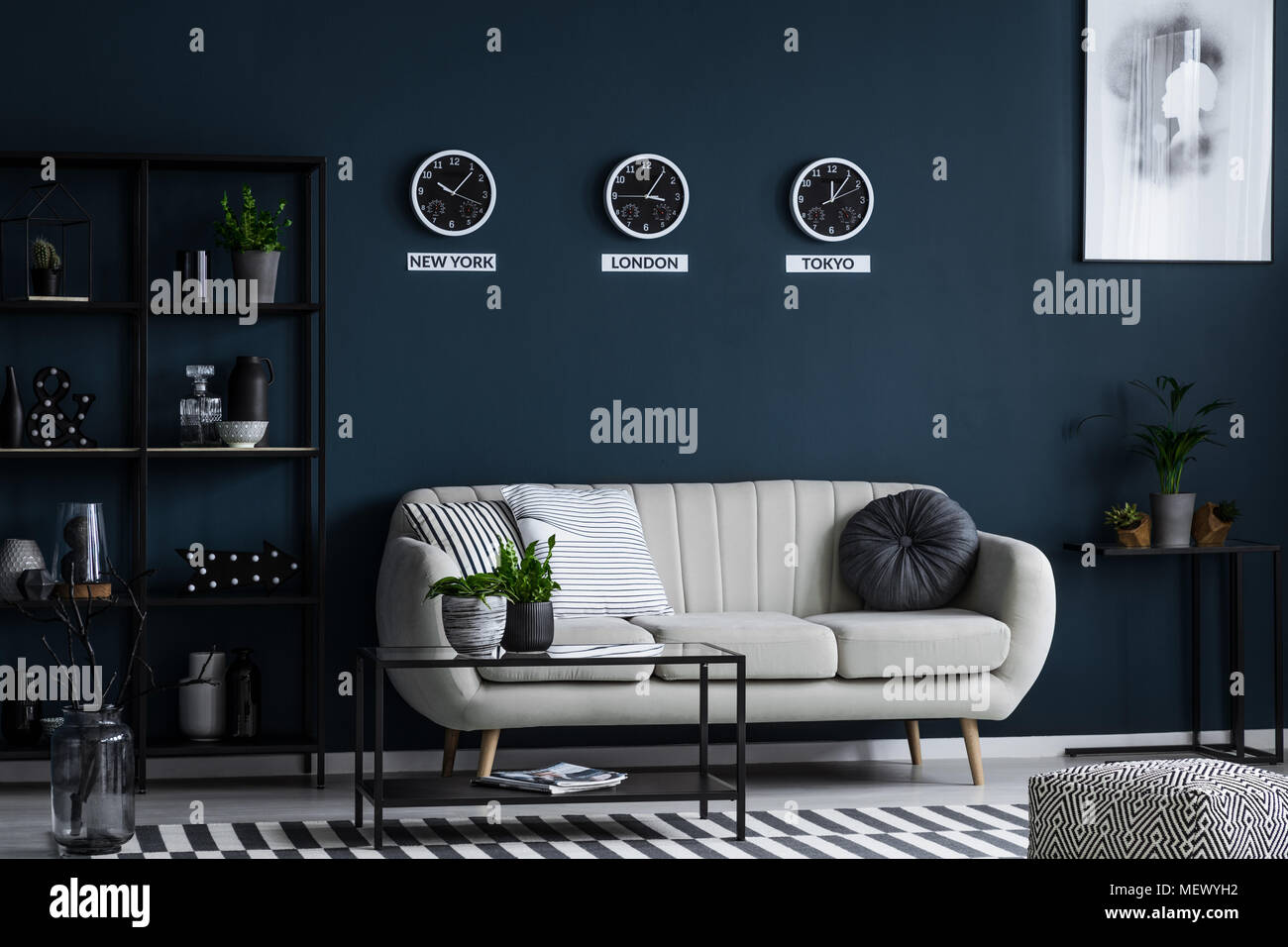 Weiß Sofa, Couchtisch, Metall Regal mit Dekorationen und drei Uhren auf der blauen Wand im Wohnzimmer Innenraum Stockfoto