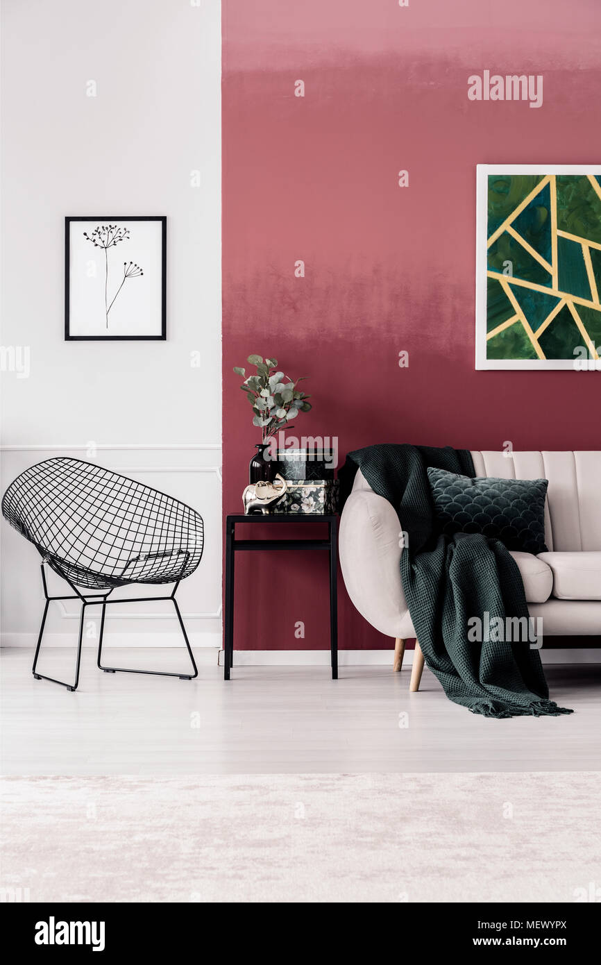 Grüne Decke auf dem Sofa gegen rote Wand mit Malerei in Wohnzimmer Einrichtung mit Sessel Stockfoto
