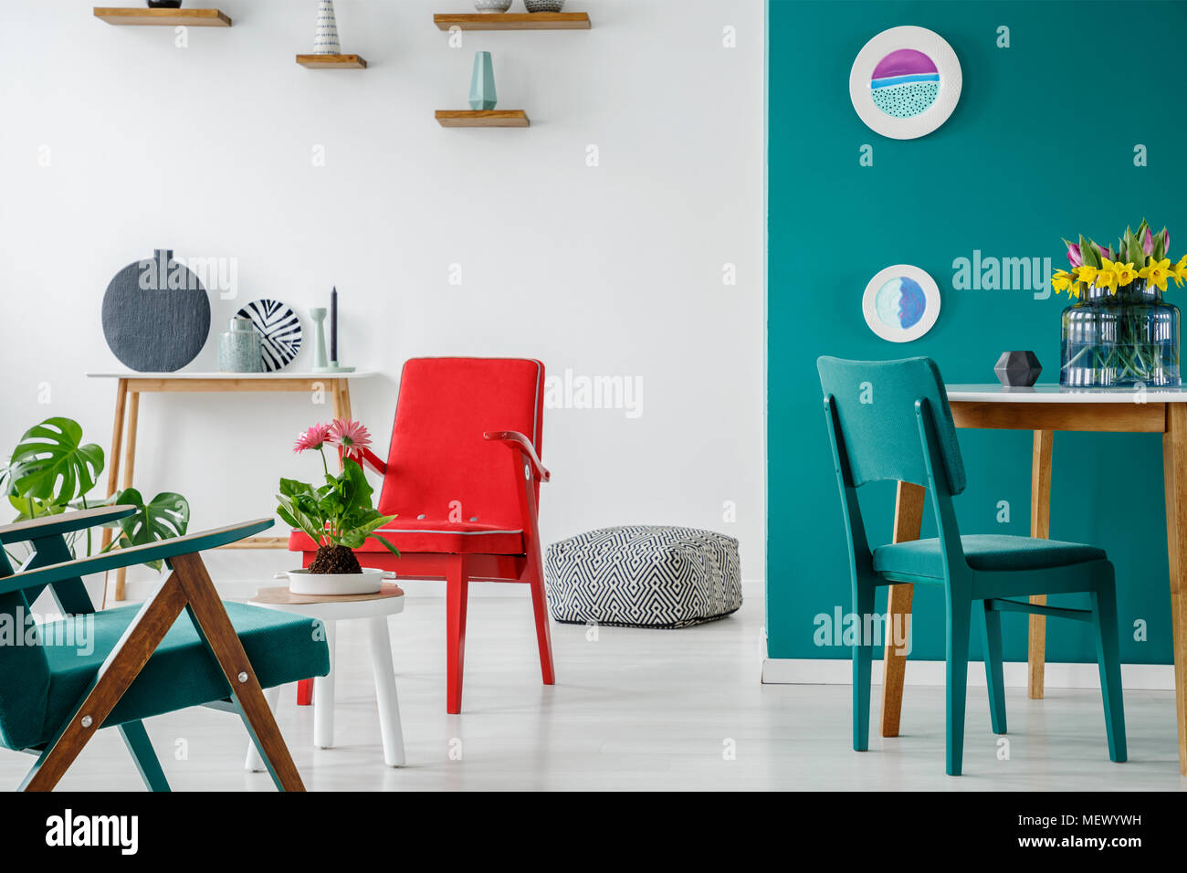 Blauen und Roten Stuhl am Tisch mit Blumen im Wohnzimmer Interieur mit Platten auf einer grünen Wand Stockfoto