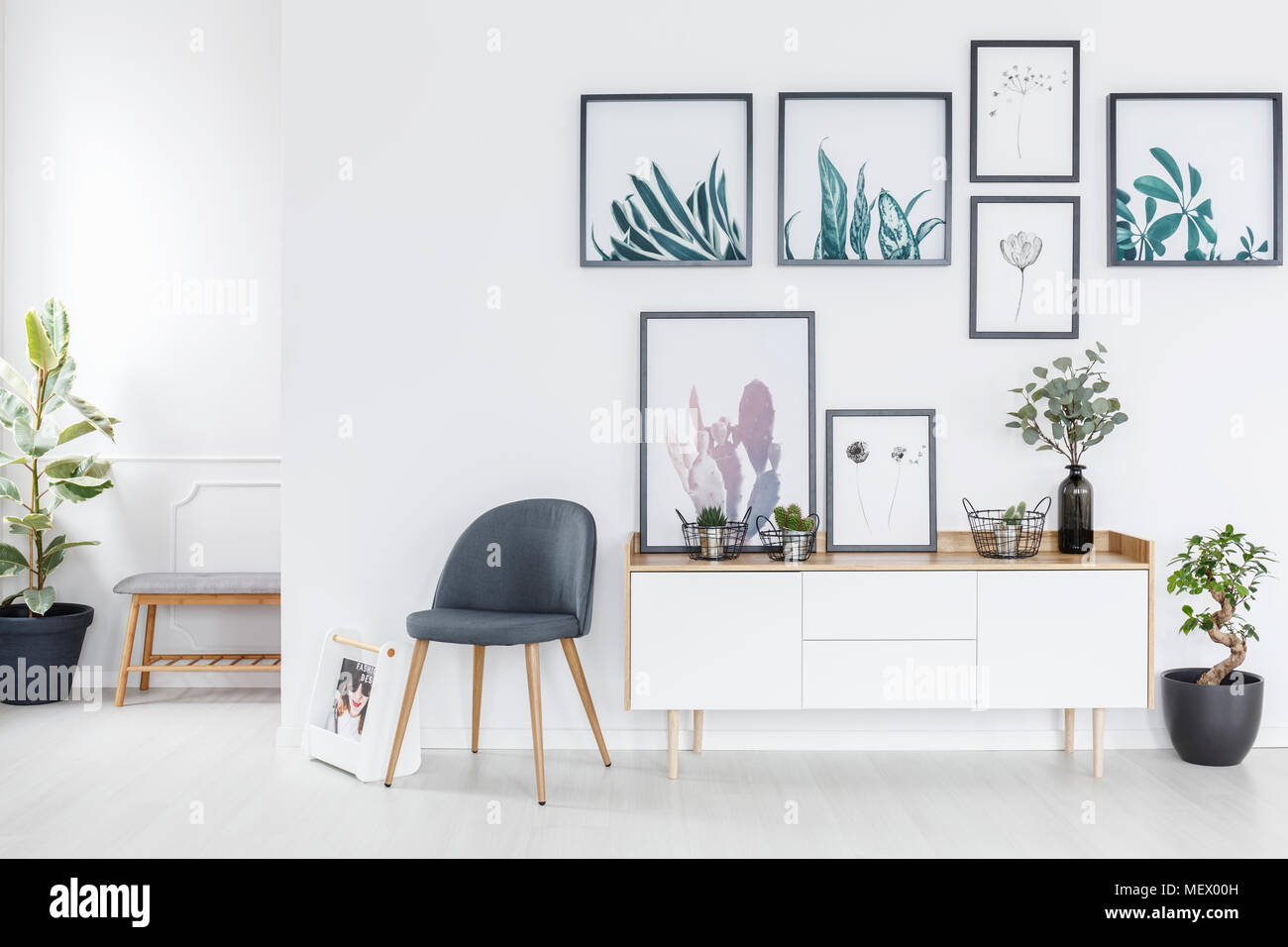 Grau Stuhl neben einem weißen Schrank mit frischen Pflanzen in hellen Innenraum mit Galerie an der Wand Stockfoto