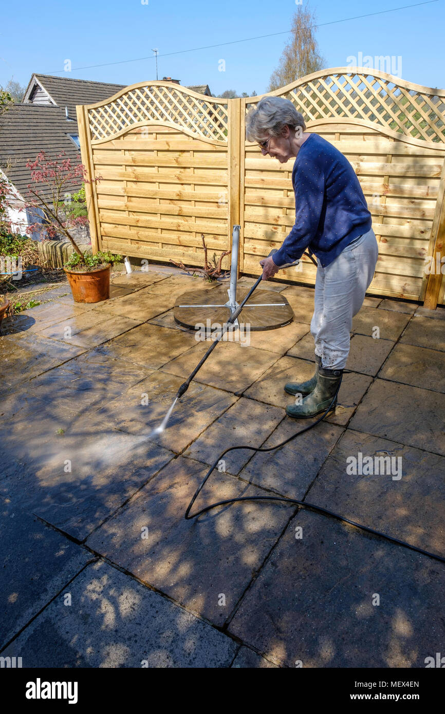 Ältere Frau spray Waschmaschine Terrasse mit Hochdruckreiniger am Anfang des Sommers in England Großbritannien Stockfoto