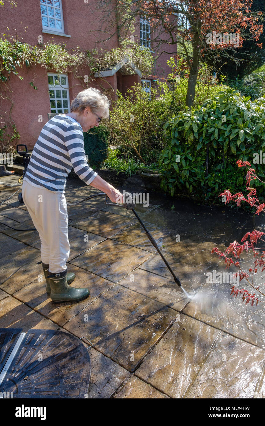 Ältere Frau SPRITZREINIGUNG Terrasse mit Hochdruckreiniger auf Garten, England UKUK. Stockfoto