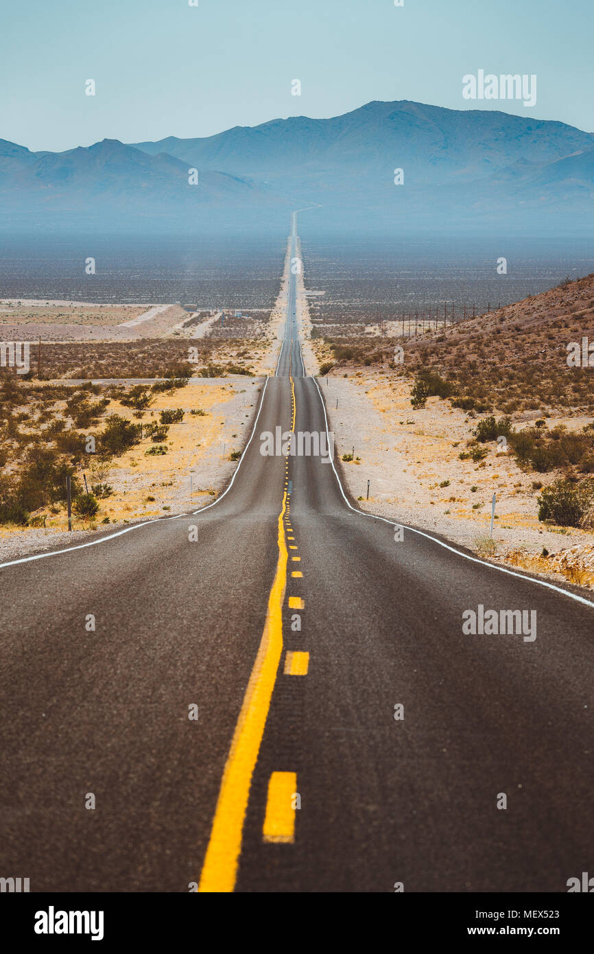 Klassische vertikale Ansicht von einem endlosen geraden Straße durch die karge Landschaft der berühmten Death Valley mit extremer Hitze Dunst im Sommer Stockfoto