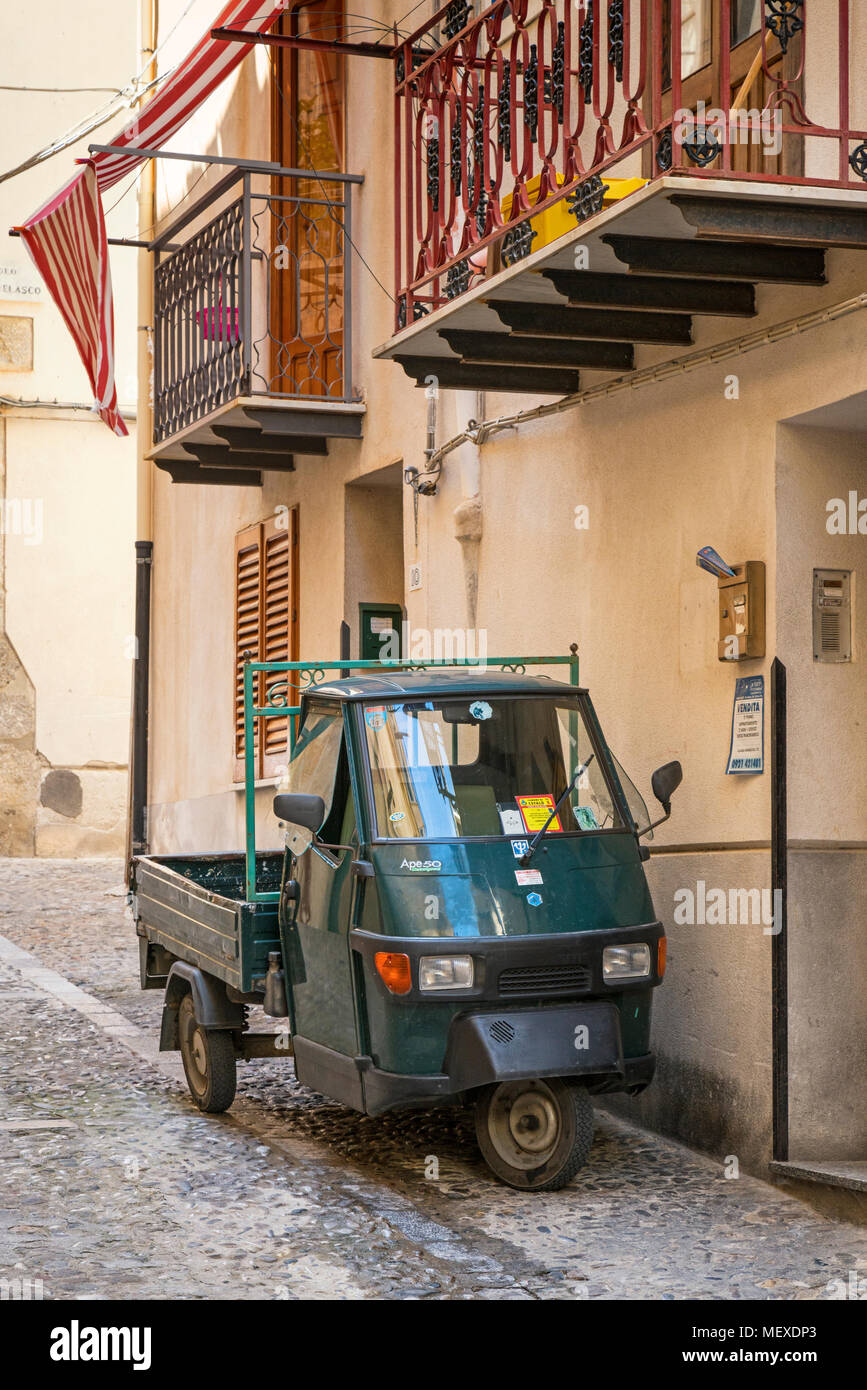 Eine alte Piaggio Ape 50 in den gepflasterten Gassen von Cefalu, Sizilien, Italien, außerhalb einige Wohneinheiten. Stockfoto