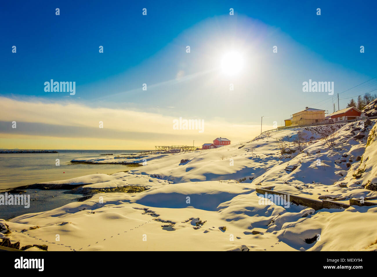 Im freien Blick auf einige Gebäude in der Bucht von Lofoten Inseln, umgeben von schneebedeckten Bergen und bunten Winter Station und Sun shinny im Himmel Stockfoto
