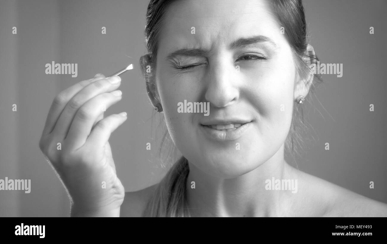 Schwarz-weiß-Porträt der jungen Frau Gefühl Schmerz nach dem Zupfen der Augenbrauen auf Spiegel Stockfoto