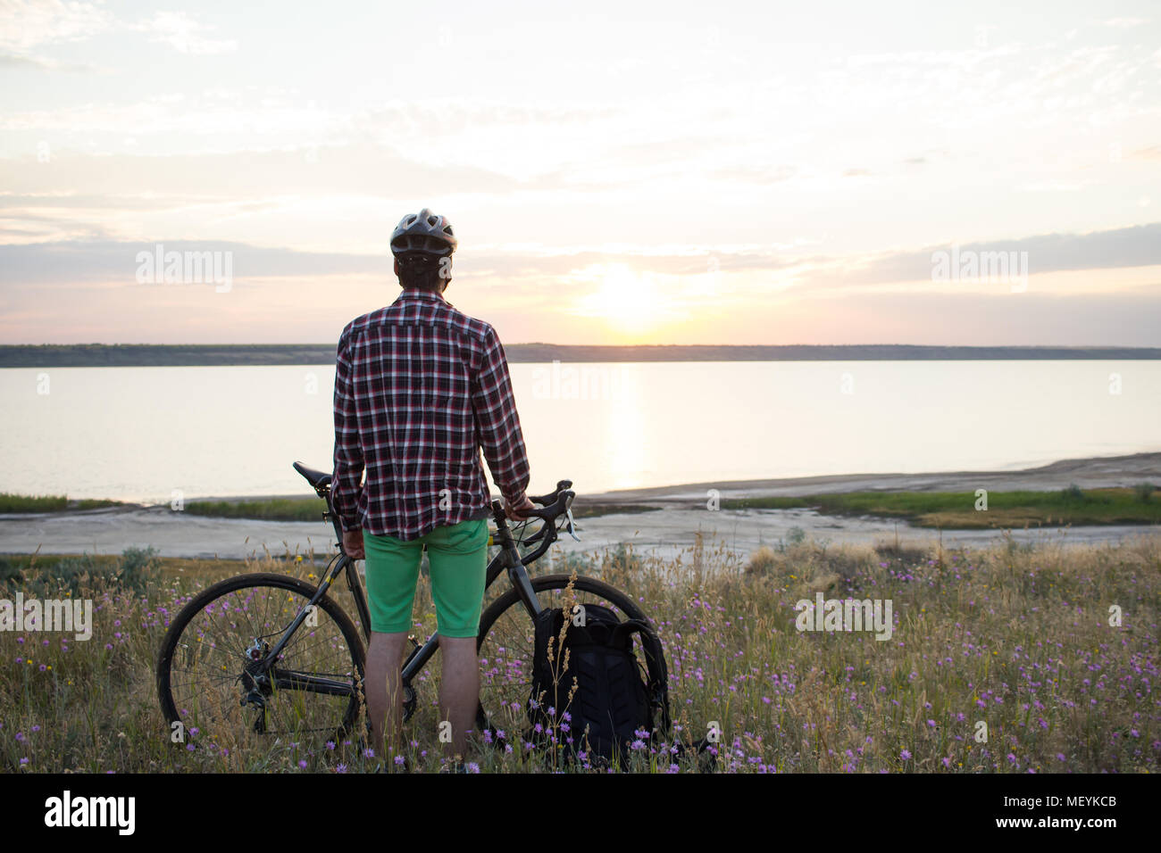 Junge männliche Fahrrad Touristen stehen auf Felsen von See againste Sonnenuntergang Stockfoto