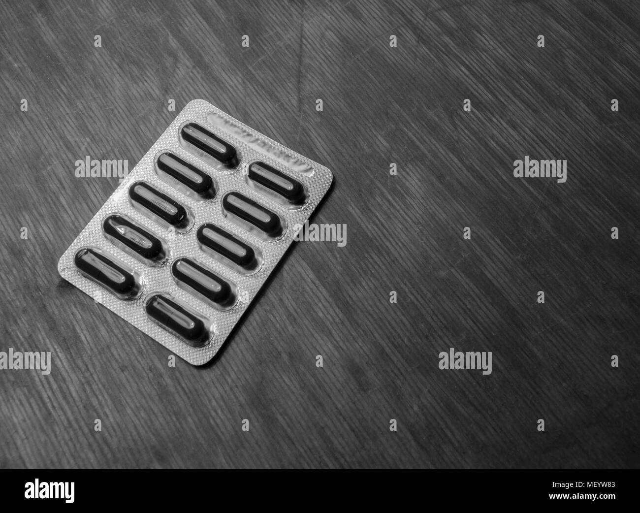 Schwarz-weiß Foto von dunklen Pillen in Blistergurt auf dem alten zerkratzt Holztisch Stockfoto