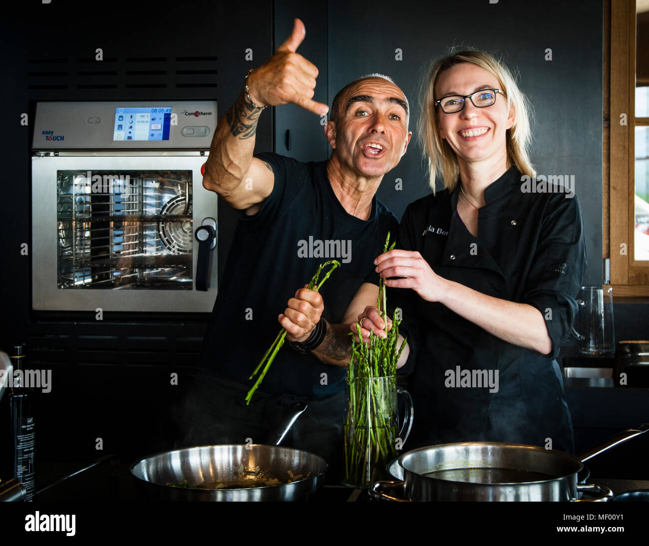 Giulio und die Journalistin Angela Berg posieren mit frisch gesammeltem Wildspargel (Asparagus acutifolius) in der Küche nahe Bagno Vignoni, Toskana, Italien. Das scherzhaft gemeinte Motto zum Start der Zubereitung: "Wenn du ruhst, rostest du" – wasche deine Hände, zieh deine Schürze an und los geht's. Stockfoto