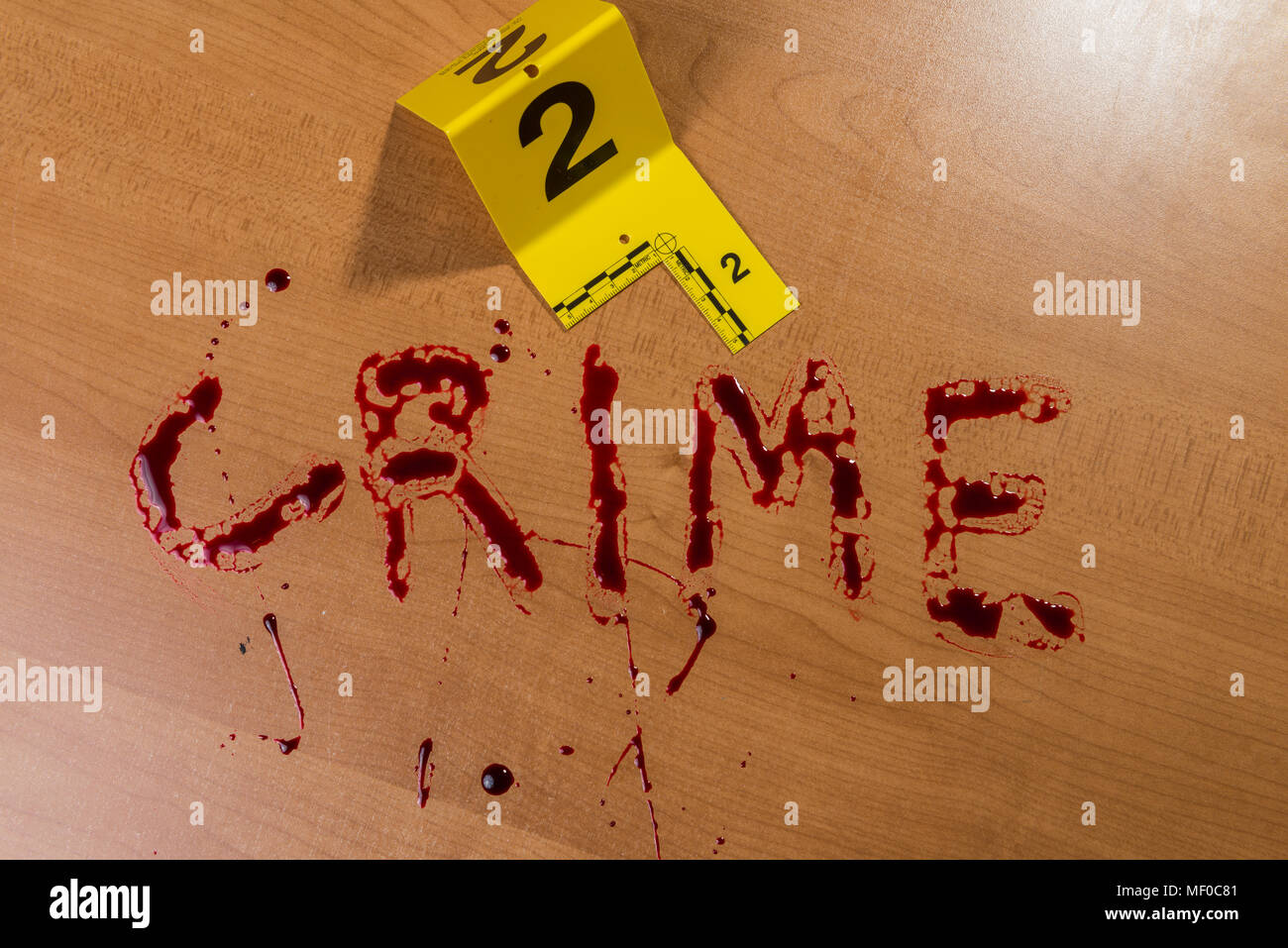 Das Wort „Verbrechen“ steht in Blut auf einer Holzoberfläche neben einem blutigen Messer, die beide durch Beweismarkierungen am Tatort gekennzeichnet sind. Stockfoto
