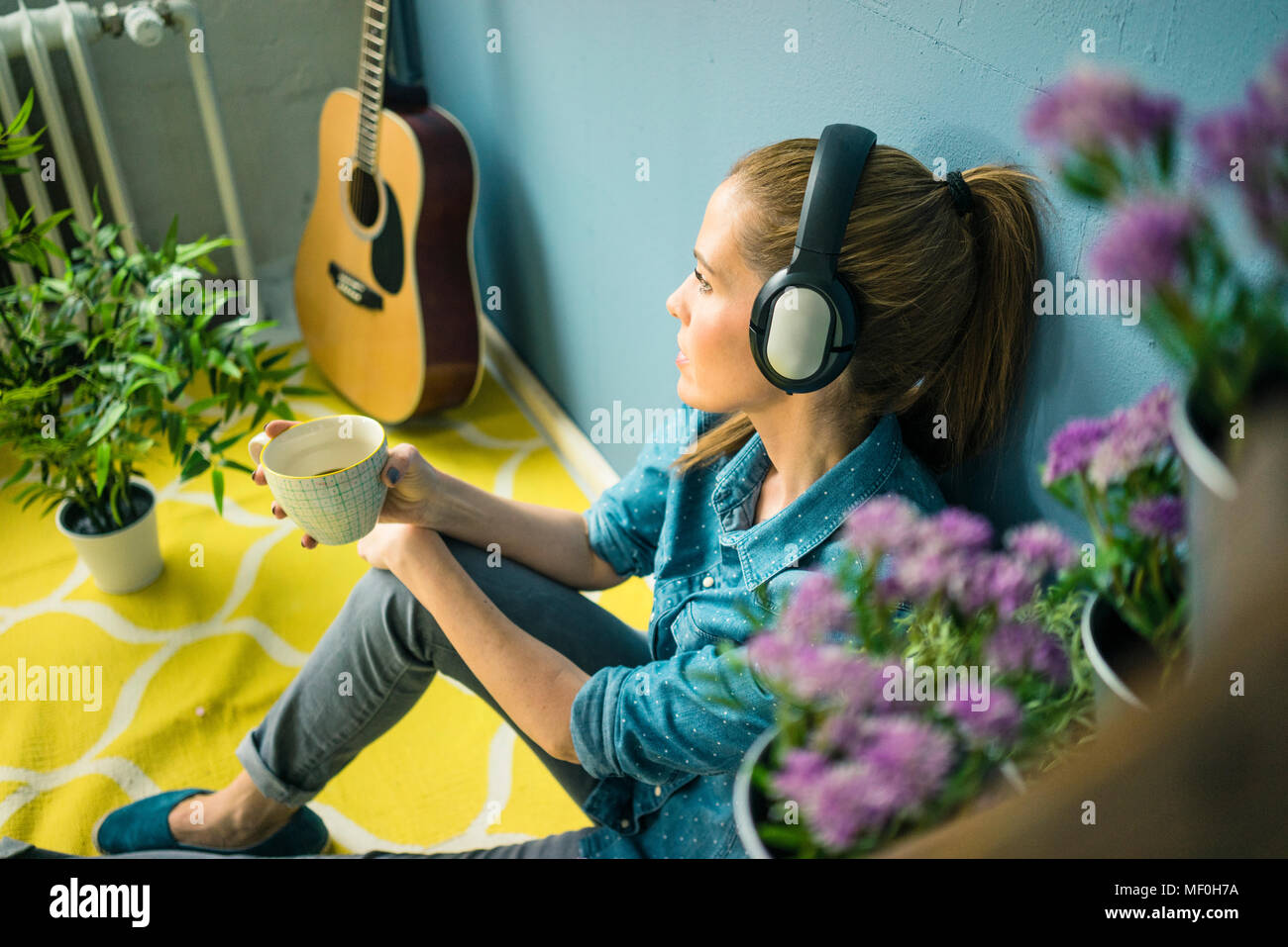 Schöne Frau in ihr Zuhause, mit Pflanzen dekoriert, Musik hören mit Kopfhörern Stockfoto