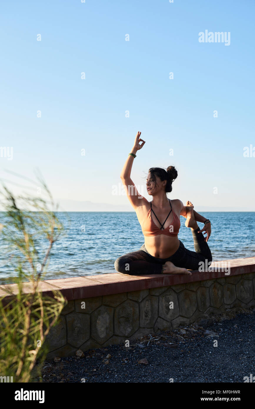 Junge Frau mit Yoga an der Wand durch das Meer Stockfoto