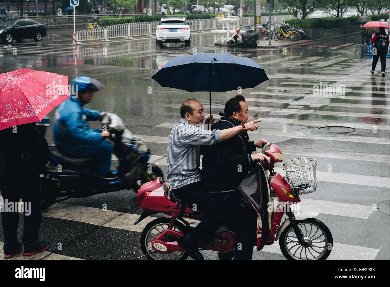 Peking, China. 21 Apr, 2018. Peking, China - April 21, 2018: Die Menschen  nehmen Unterschlupf unter einem Regenschirm, wie Sie sich einen Roller im  Regen fahren. Donat Sorokin/TASS Credit: ITAR-TASS News Agentur/Alamy