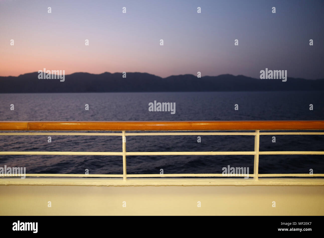 Blick vom Deck eines Kreuzfahrtschiffes in der Dämmerung in Richtung Küste. Es ist pink und lila Farben in den Himmel über einem ruhigen Meer. Stockfoto