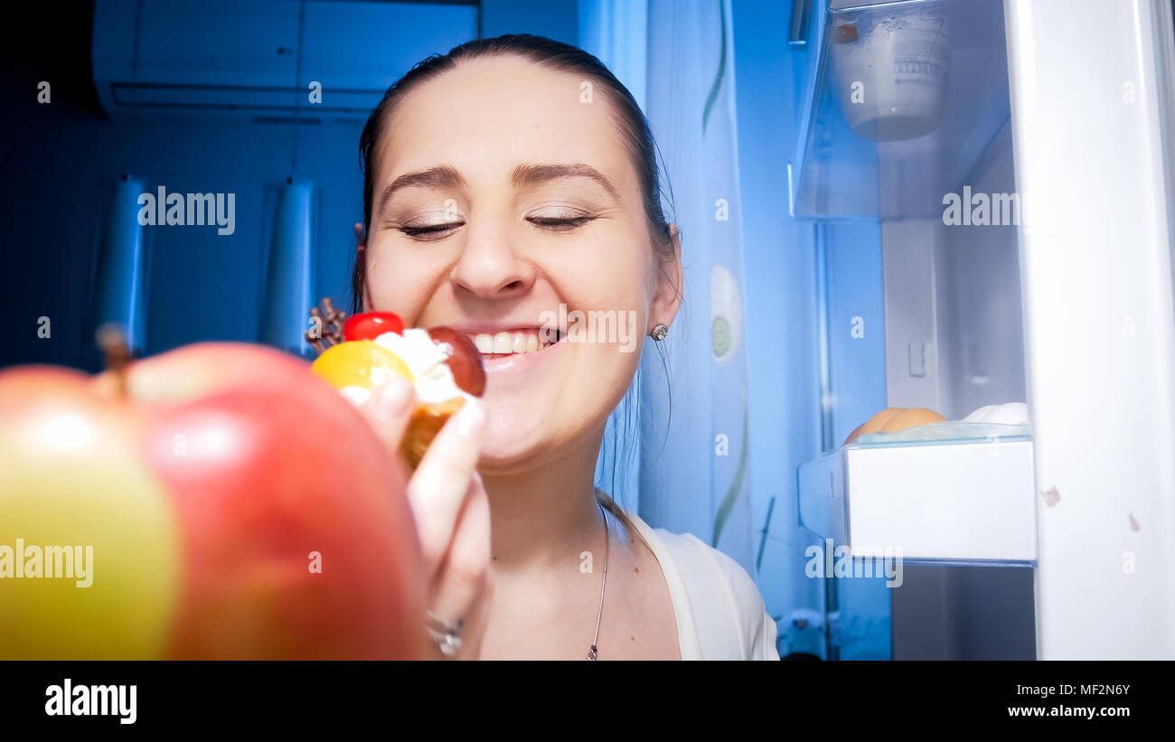 Portrait von Glücklich lächelnde Frau mit süßen Kuchen aus dem Kühlschrank in der Nacht Stockfoto