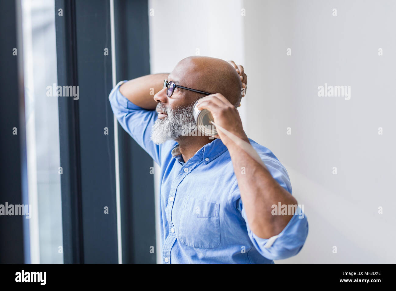 Geschäftsmann Blick aus Fenster während der Verwendung von Zinn Telefon kann Stockfoto