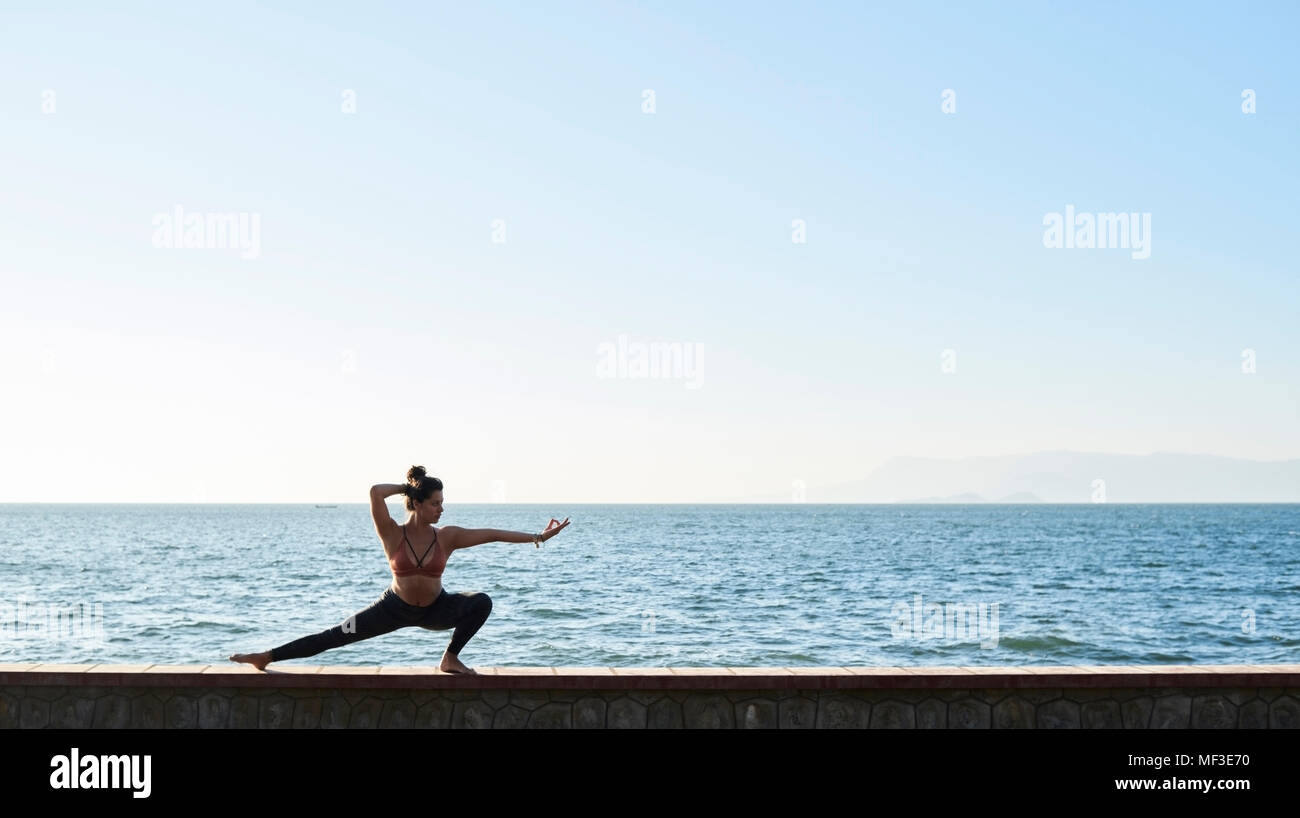 Junge Frau mit Yoga an der Wand durch das Meer Stockfoto