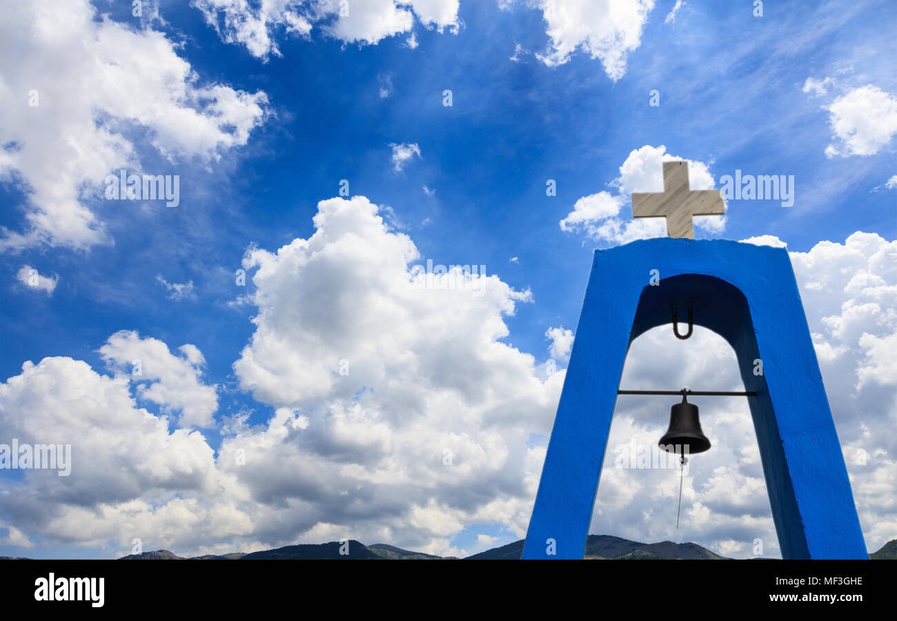 Der Kirchturm in Griechenland. Kreuz auf top und darunter. Weiße Wolken am blauen Himmel über den Bergen im Hintergrund, Copyspace Stockfoto