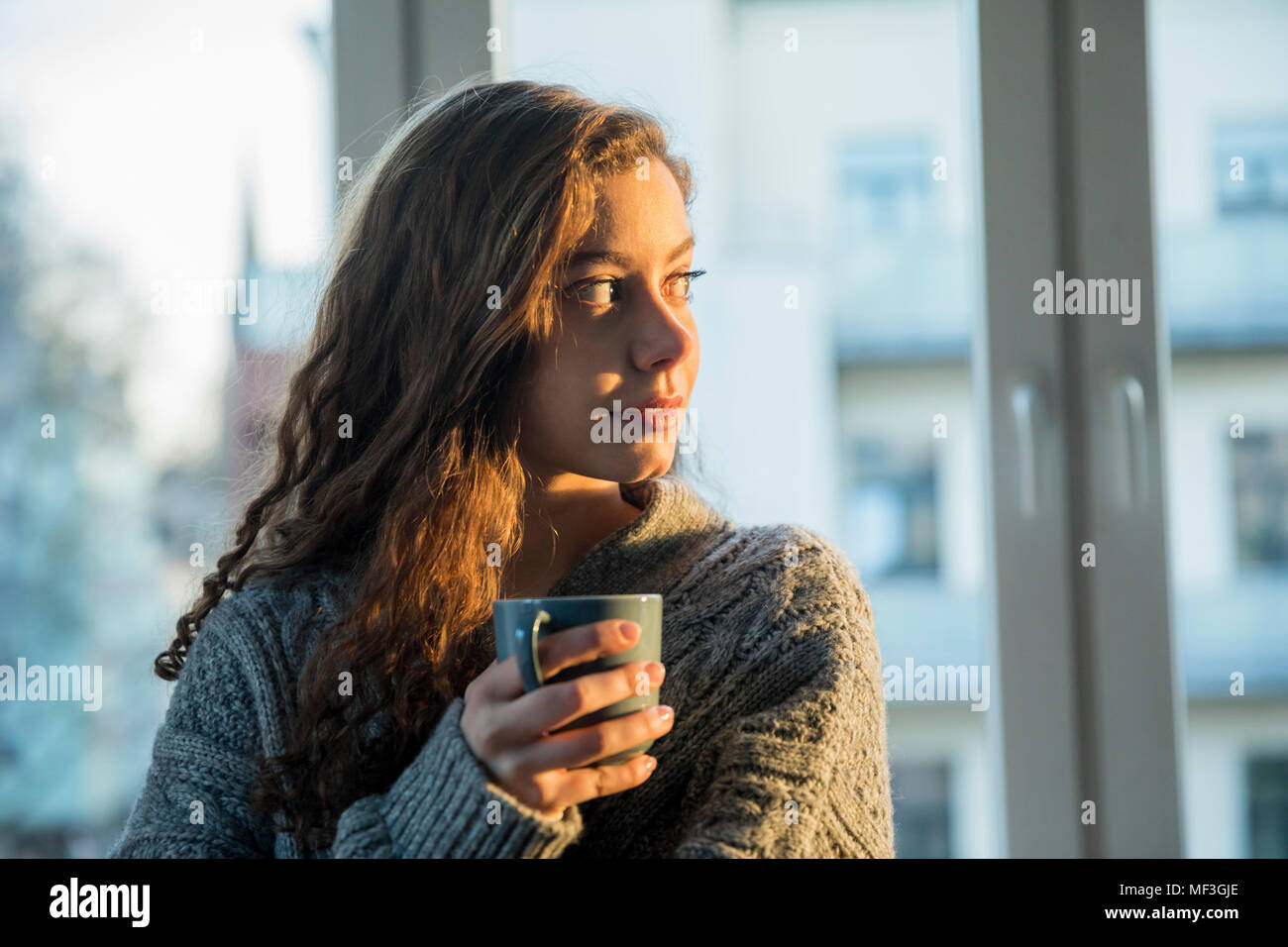 Portrait von jugendlichen Mädchen mit kaffeebecher Blick aus Fenster am Abend Stockfoto