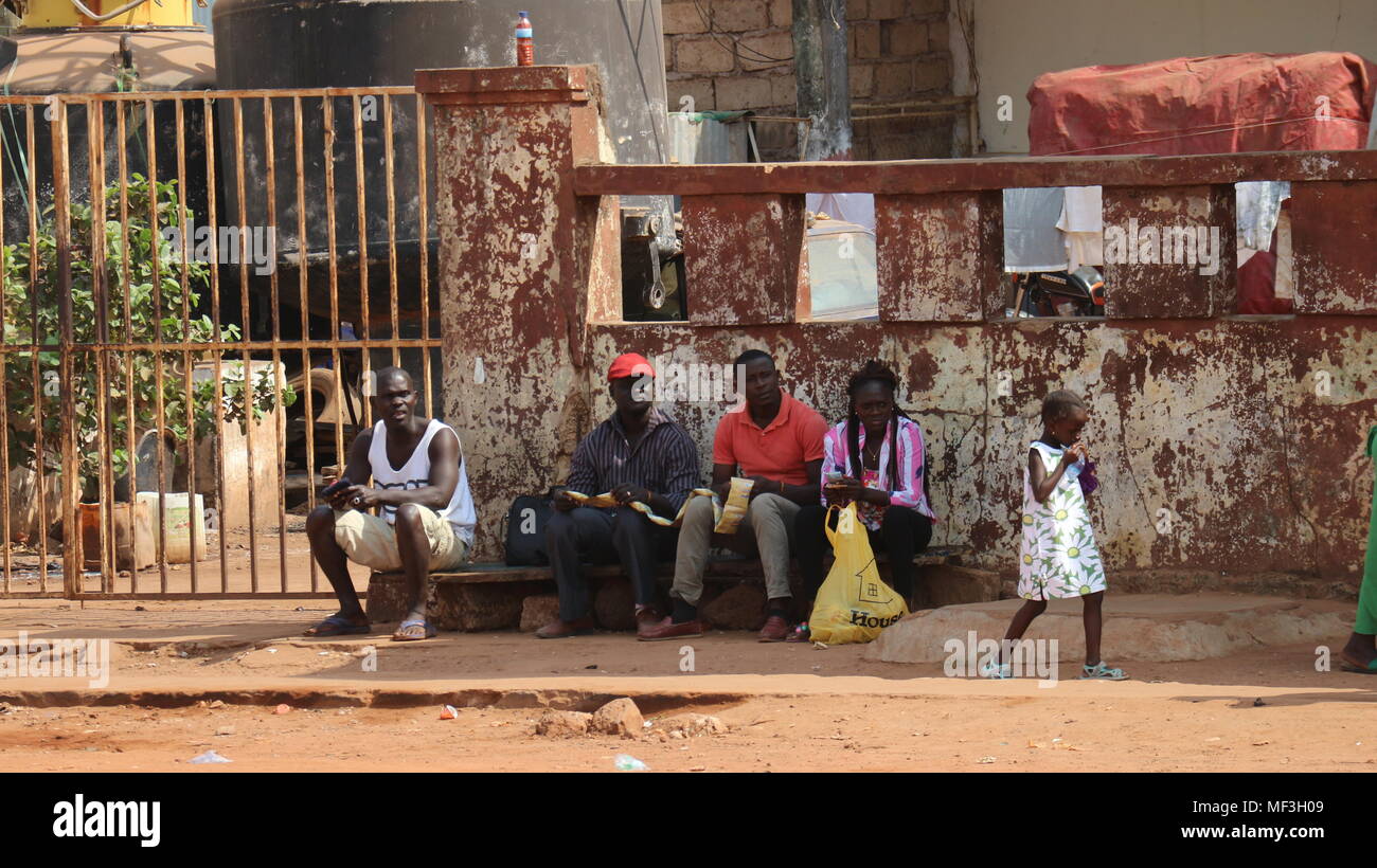 Menschen, die auf der Seite der Straße vor einem alten Gebäude in Bissau, Guinea-Bissau, Westafrika sitzen. Stockfoto