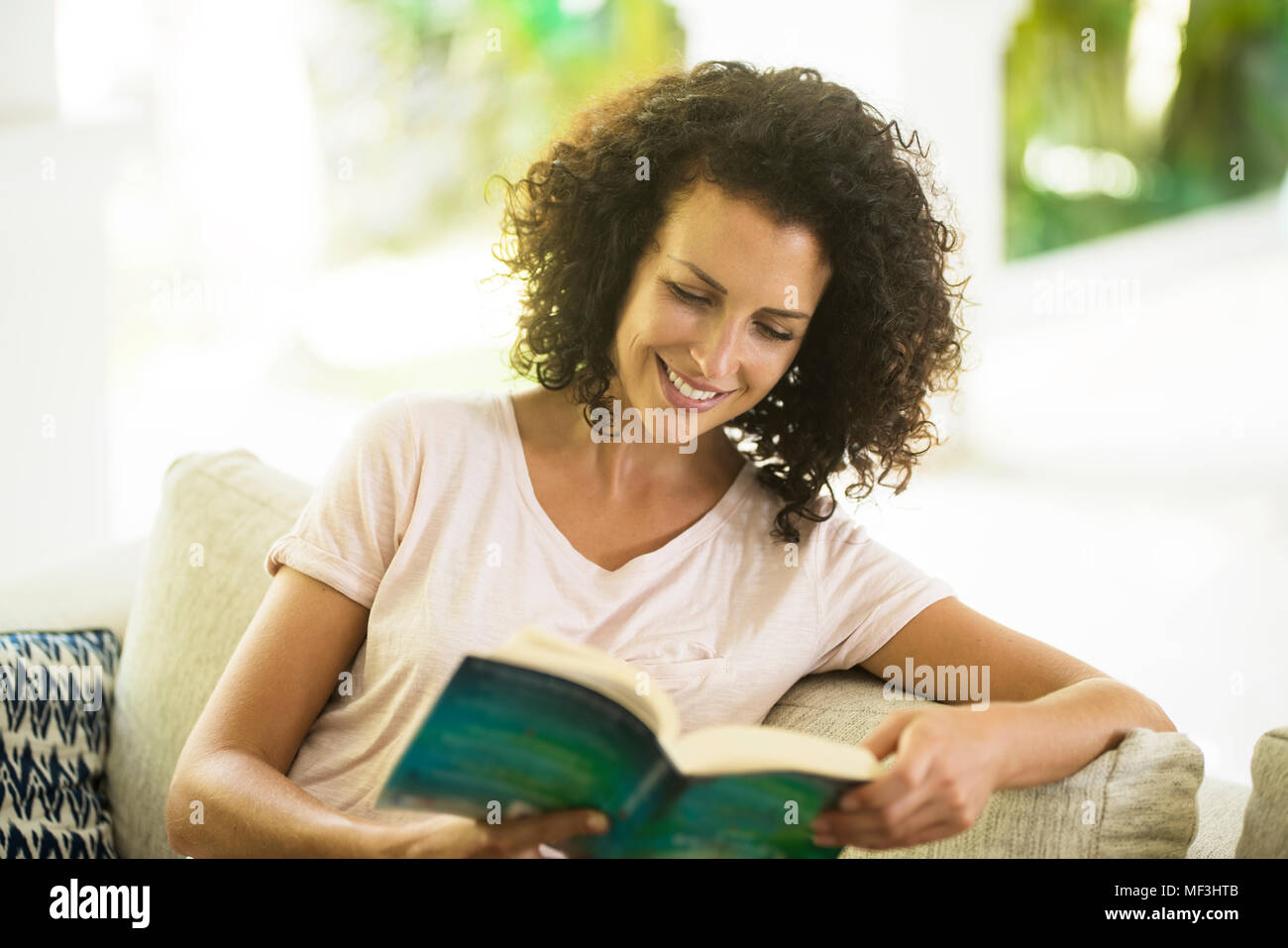 Lächelnde Frau mit lockigem Haar ein Buch lesen Stockfoto
