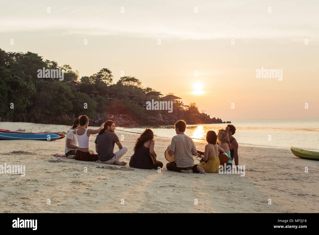 Thailand, Koh Phangan, Gruppe von Menschen sitzen auf einem Strand mit Gitarre bei Sonnenuntergang Stockfoto