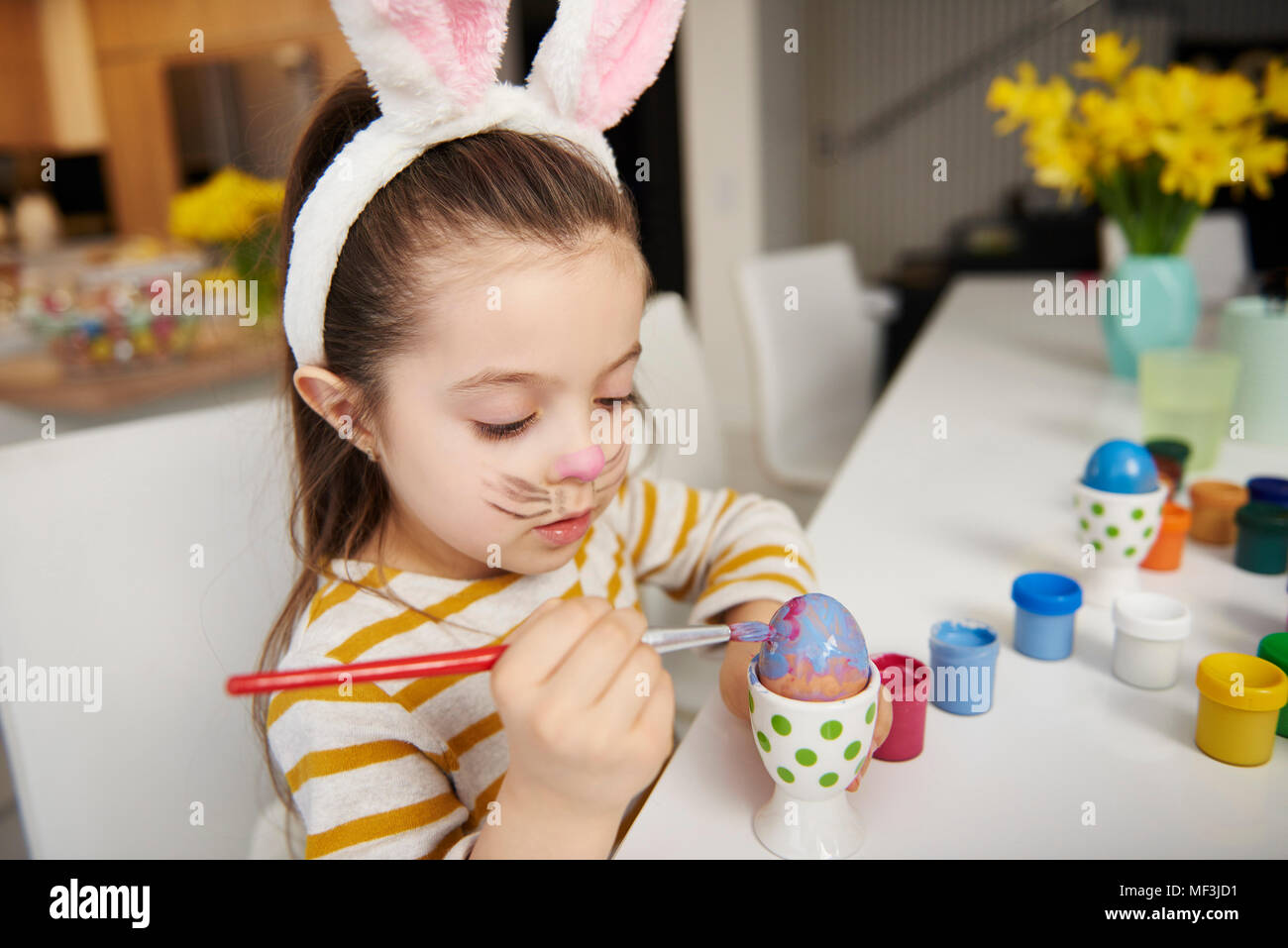 Mädchen mit Hasenohren am Tisch Malerei Ostereier sitzen Stockfoto