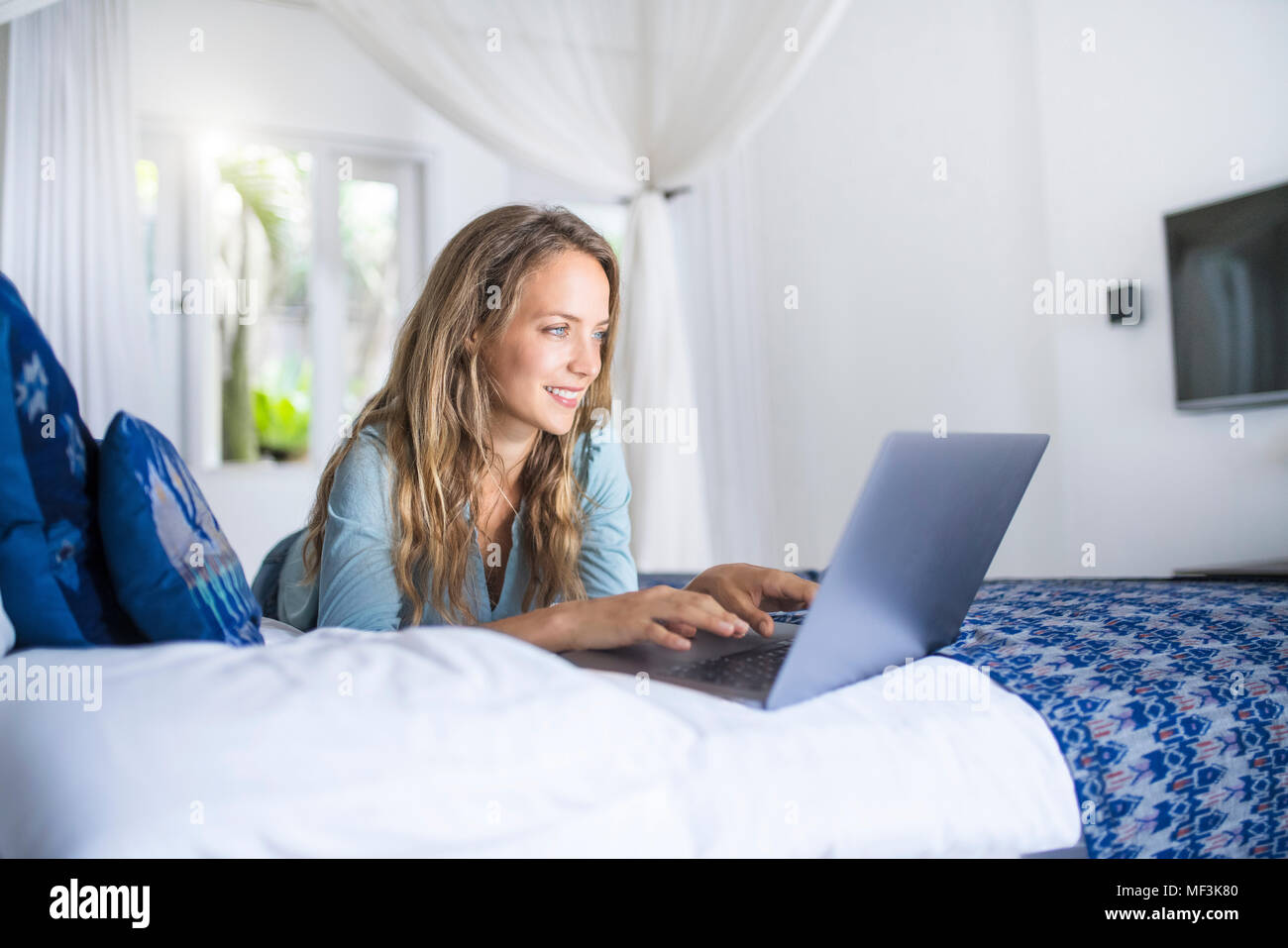 Lächelnde Frau im Bett liegend mit Laptop Stockfoto