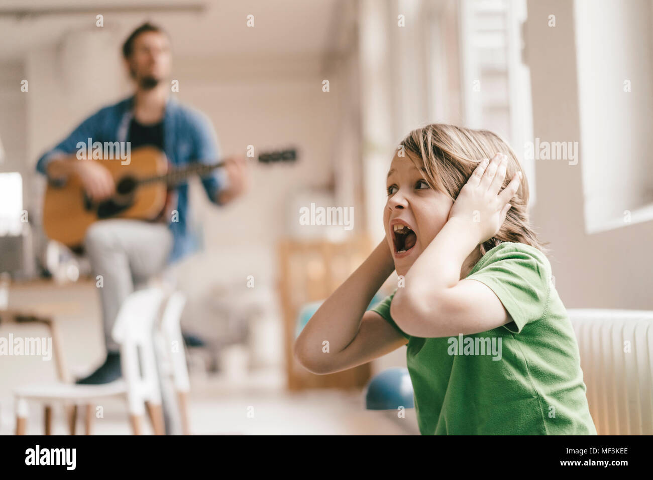 Sohn entsetzt über seine Ohren mit Vater Gitarre spielen zu Hause Stockfoto