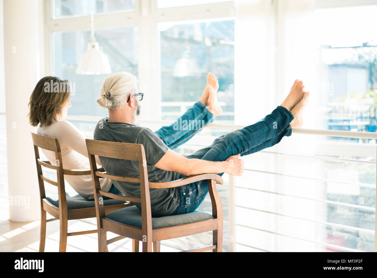 Entspannt reifes Paar zu Hause sitzen auf Stühlen mit Füßen bis Stockfoto