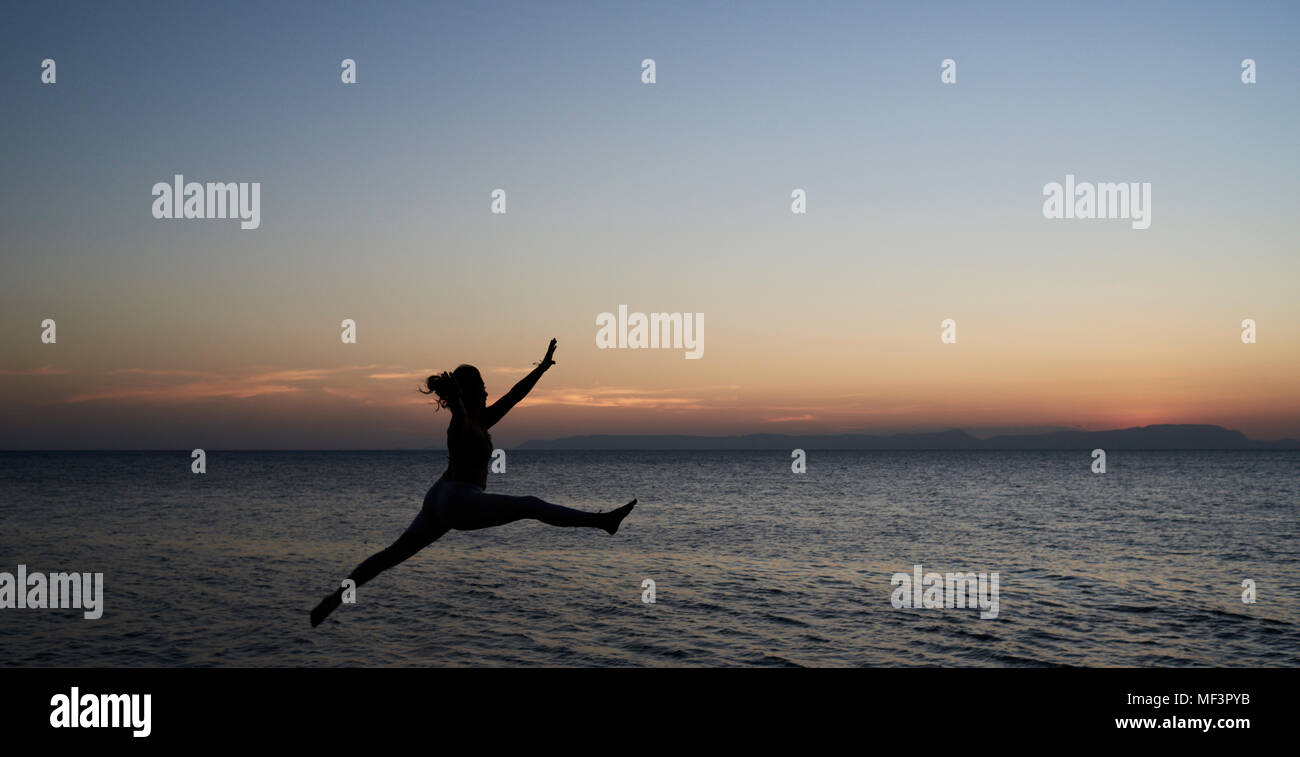 Junge Frau am Meer bei Sonnenuntergang springen Stockfoto