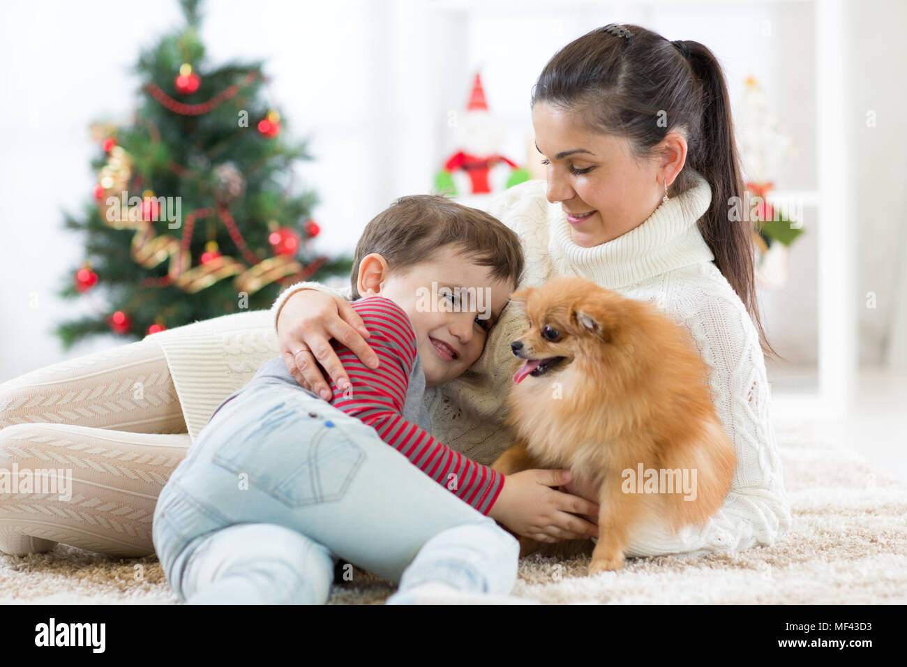 Familie Mutter und Sohn spielen mit Hund am Weihnachtsbaum Stockfoto