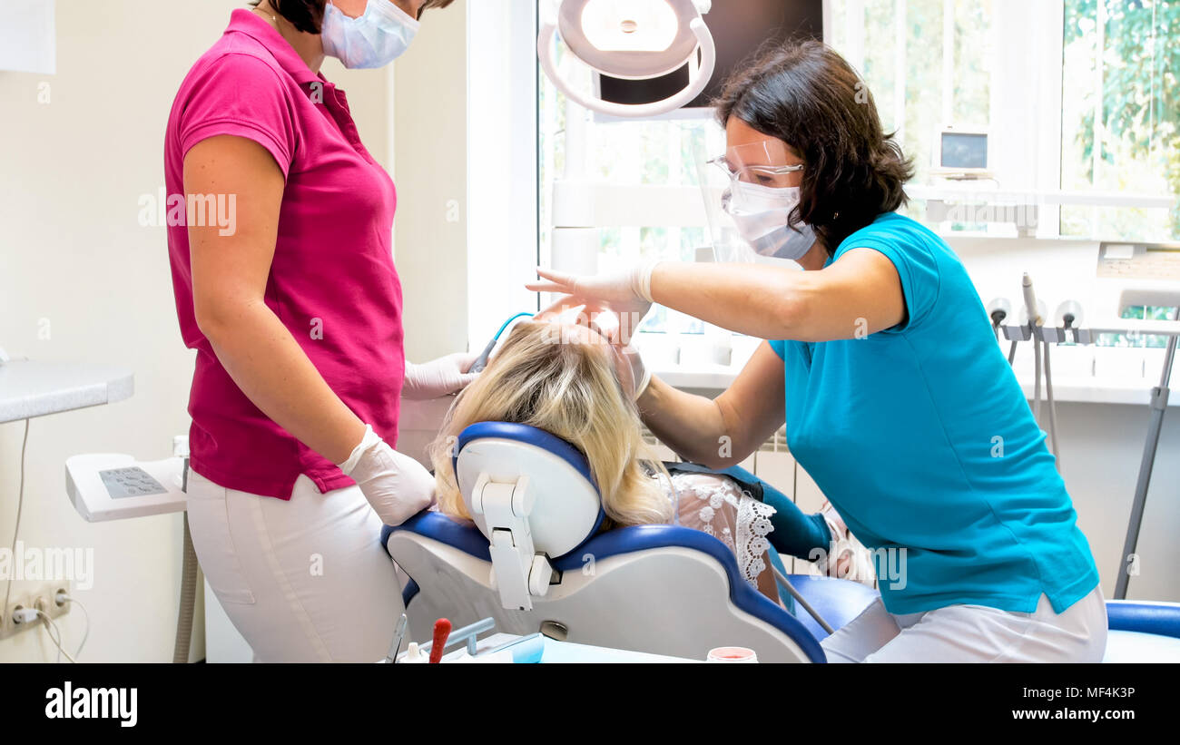 Zahnarzt in portective Maske und Brille treting Patientin Stuhl Stockfoto