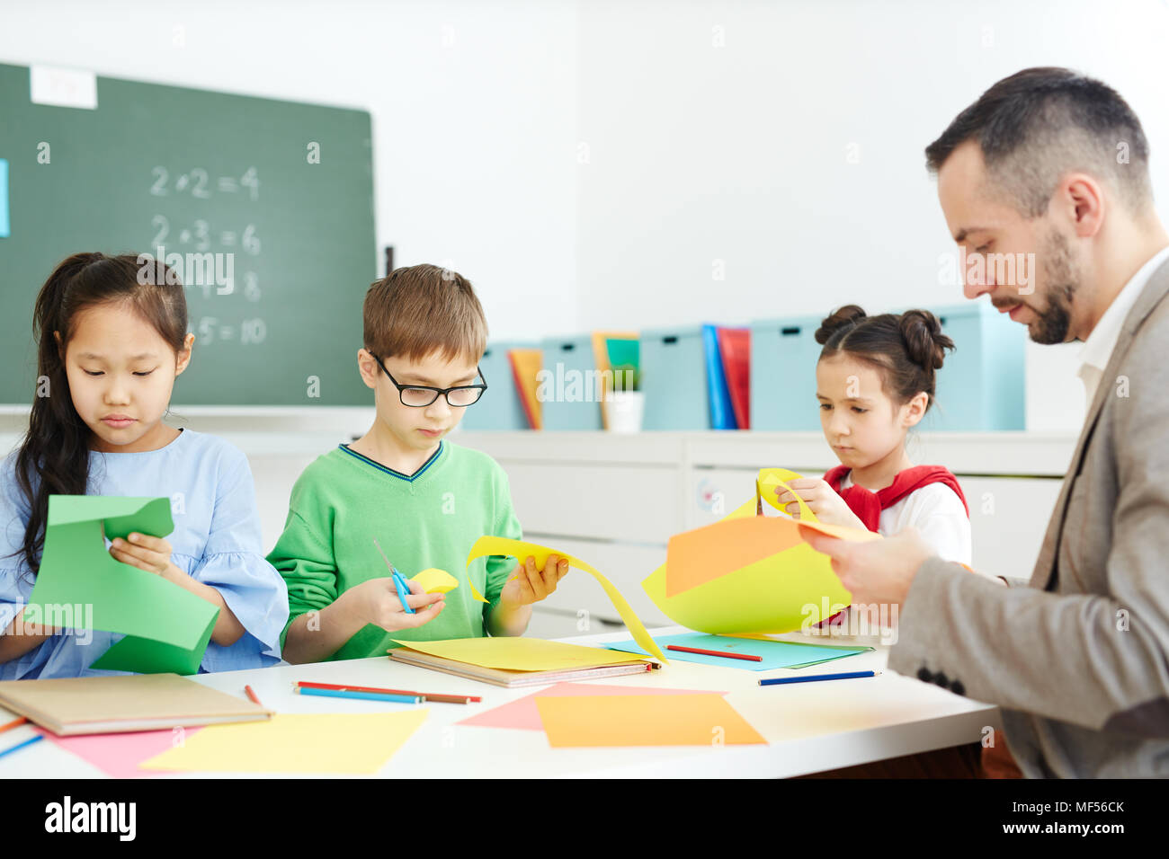 Grundschule Kinder Im Klassenzimmer Sitzen Und Origami Mit Mannlichen Lehrer Wahrend Sie Nach Der Schule Kunst Klasse Stockfotografie Alamy