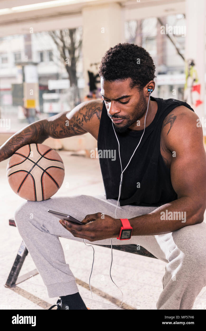 Mann mit Tattoos und Sie ihr Smartphone- und Ohrhörer Basketball Stockfoto