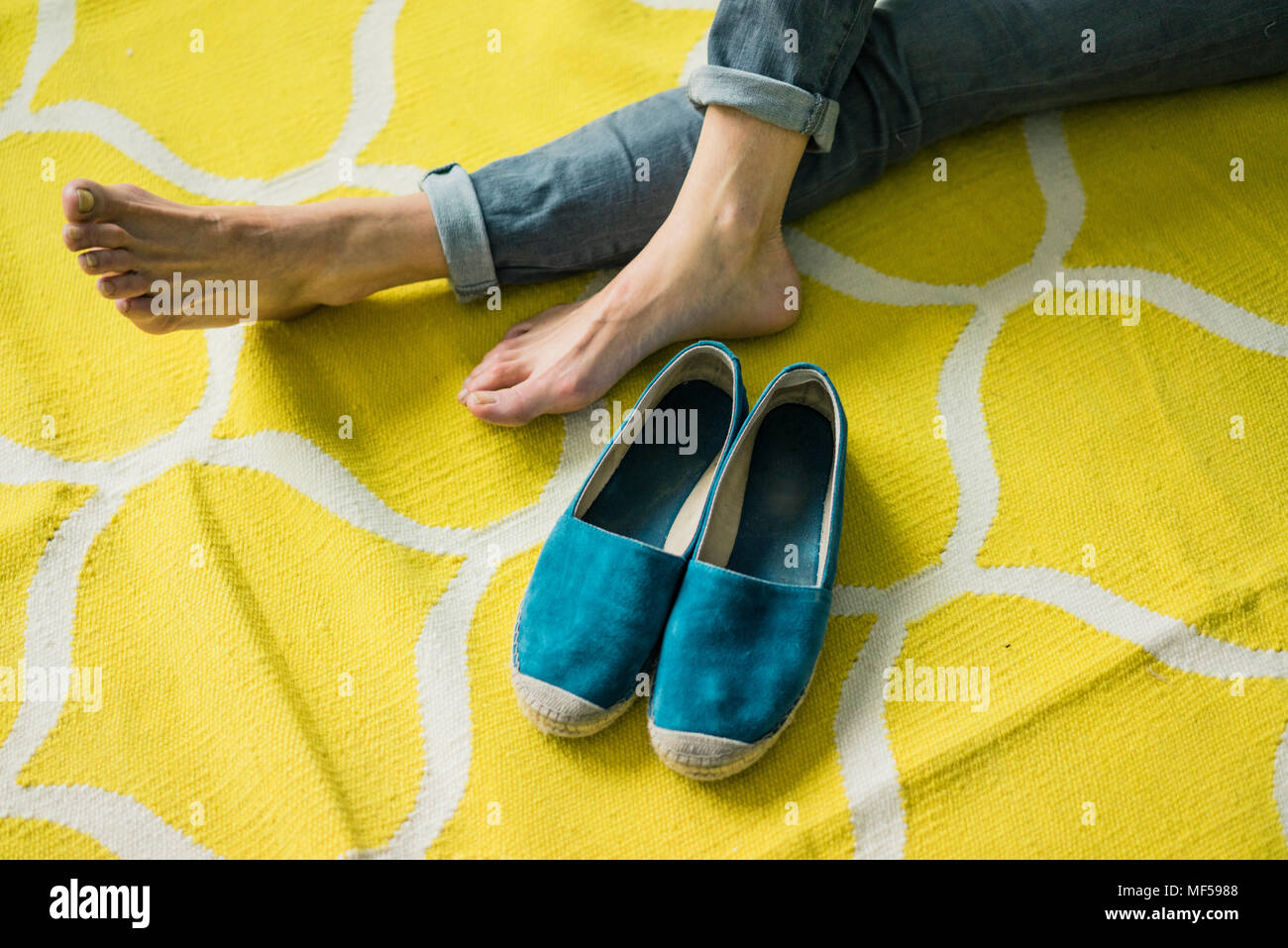 Füße und Schuhe der Frau, entspannend auf einem gelben Teppich Stockfoto